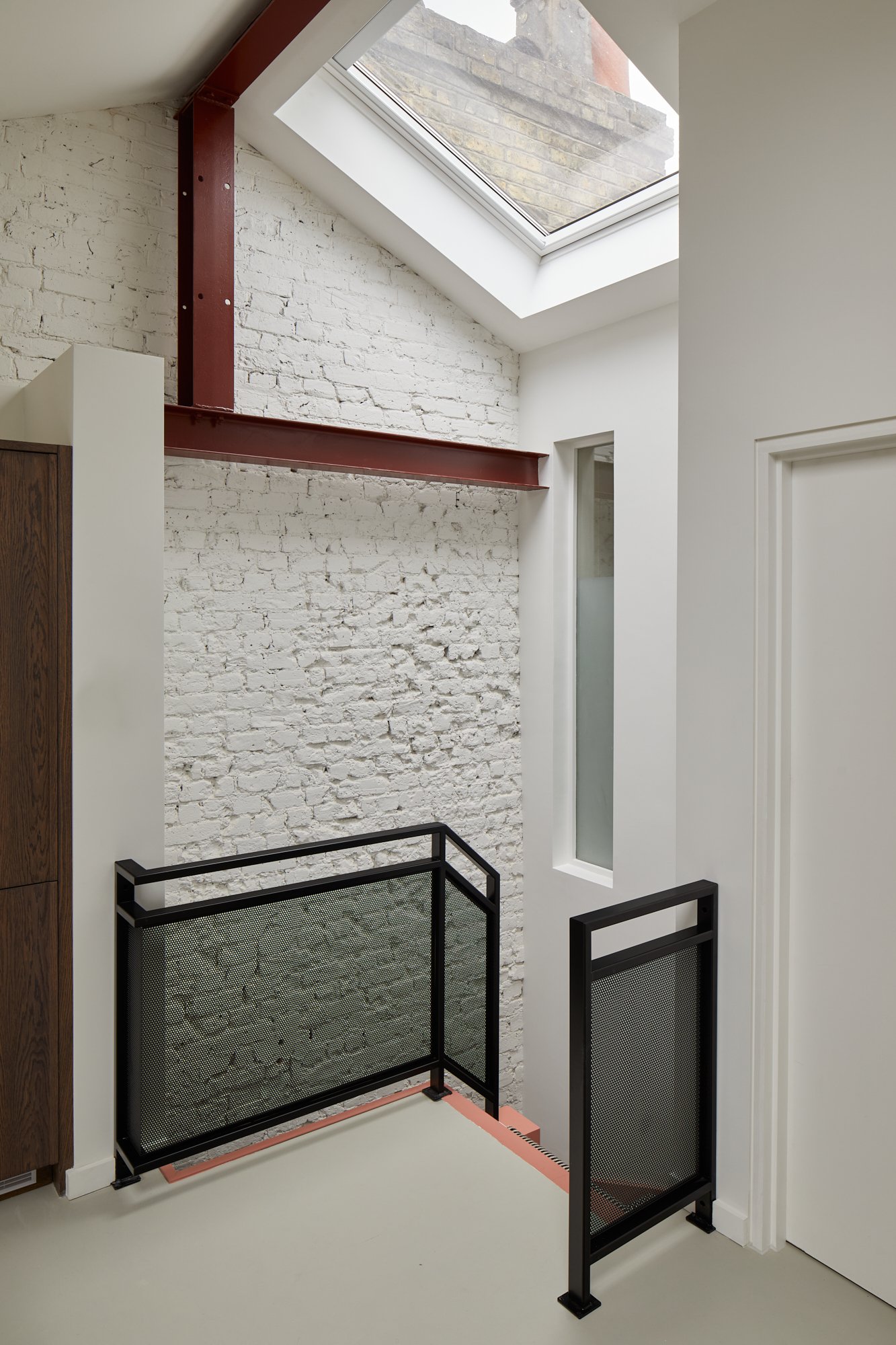 White exposed brick wall with custom black metal banisters, skylights cover the ceiling and custom red steel beams London SW1V
