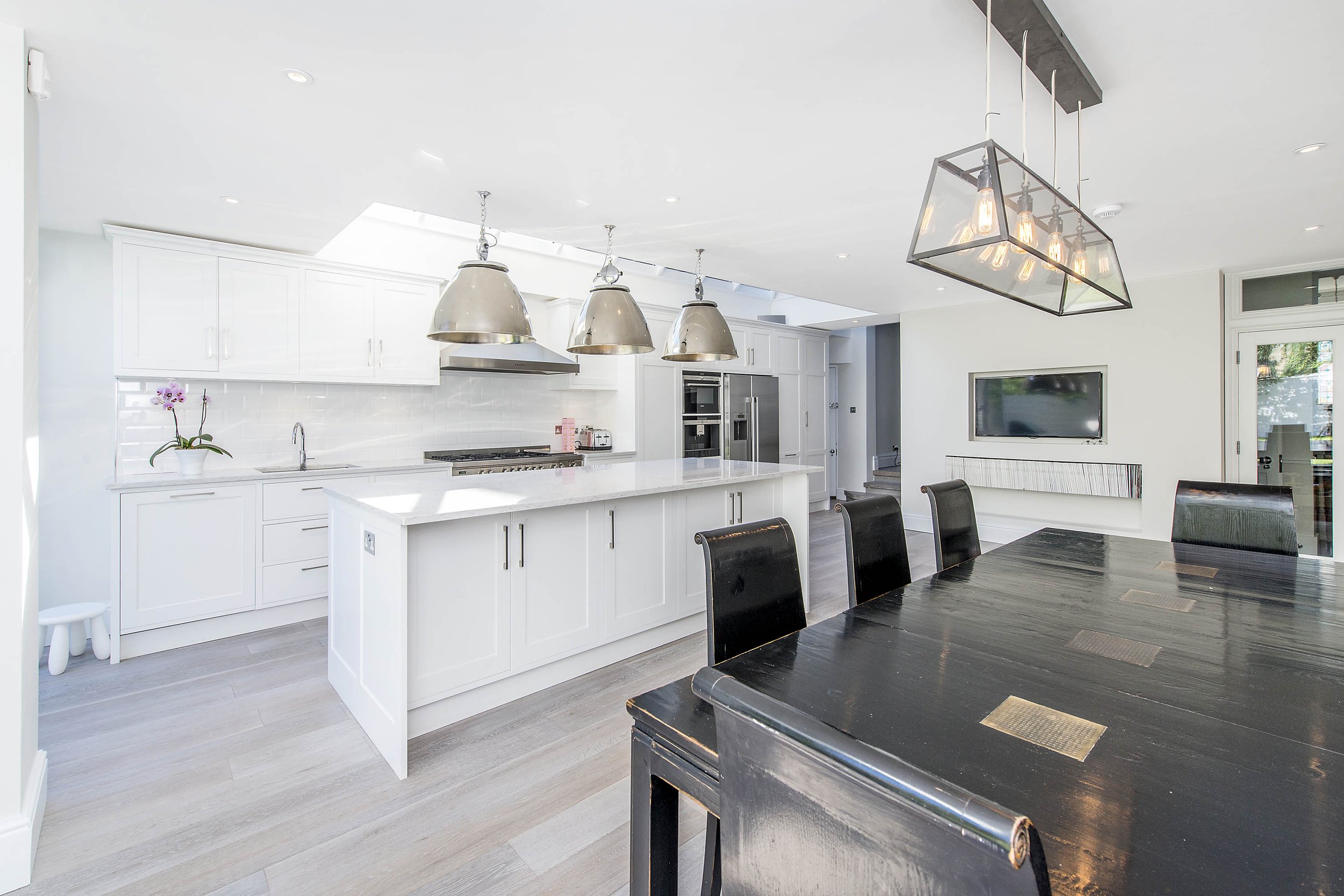 Three metallic pendant lights illuminate the space, which boasts hardwood floors. A bright, modern kitchen with white cabinets and a large island featuring a marble countertop. Stainless steel appliances complement this modern home and the dark table