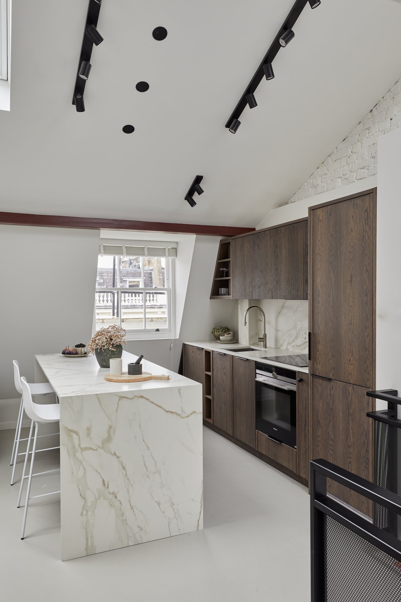 Marble waterfall white kitchen island in custom dark wood open plan kitchen in london SW1V