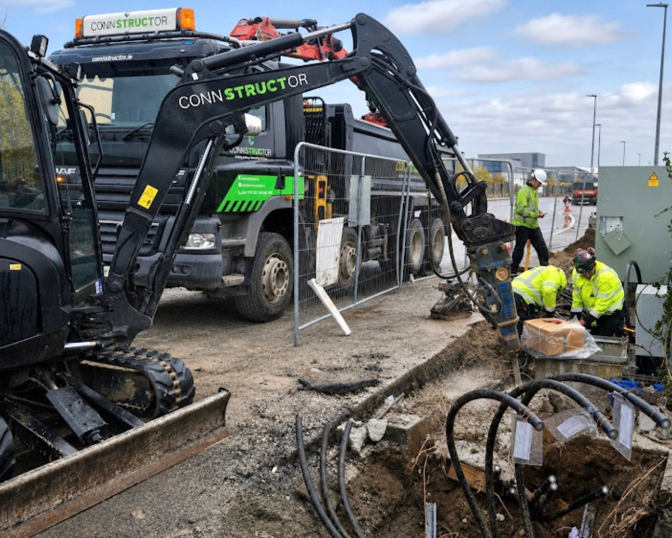 Construction workers digging underground utilities at a construction site with heavy machinery.