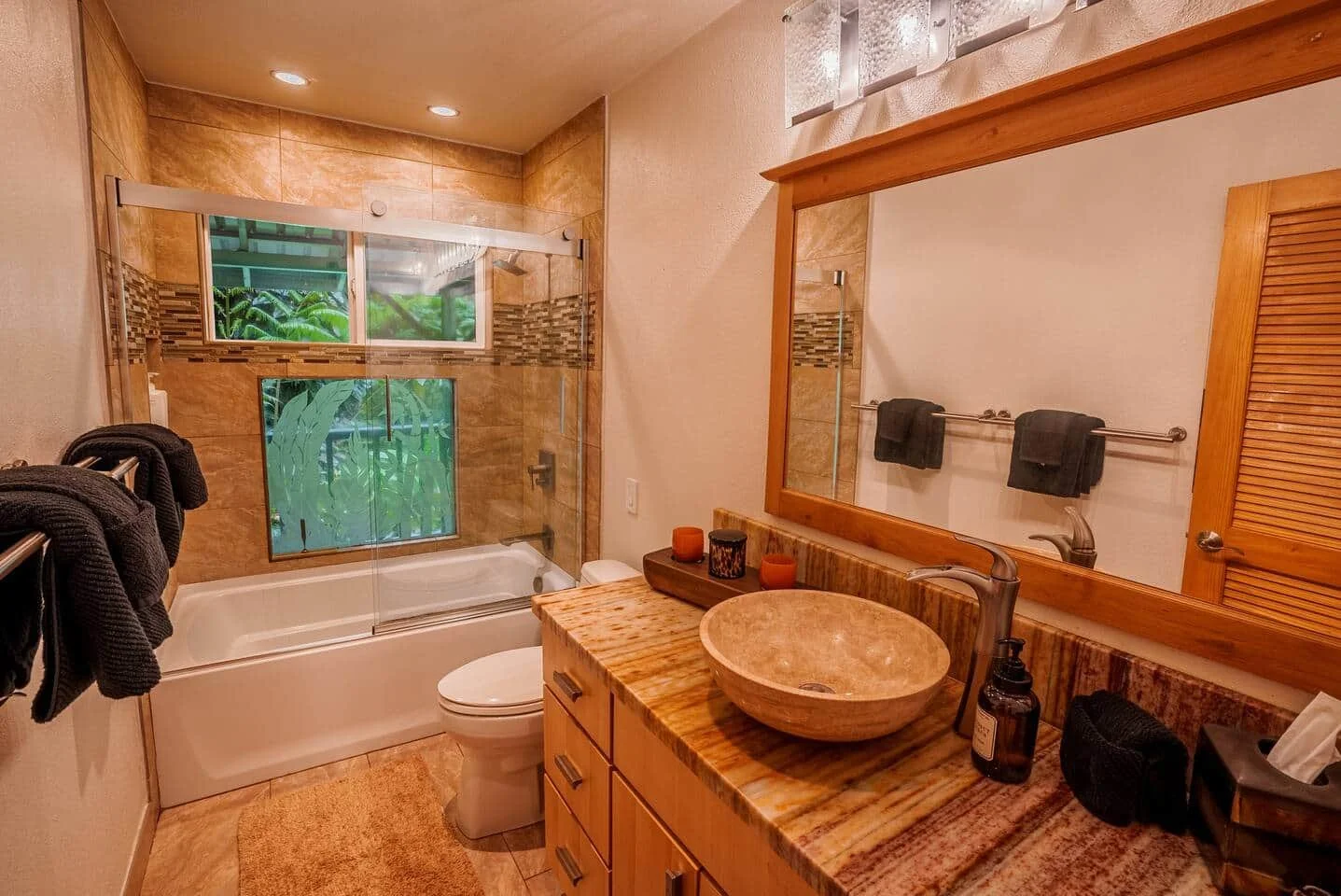 Bathroom with a bathtub and shower area, a wooden vanity with a vessel sink, a large mirror, and black towel hooks on the wall.