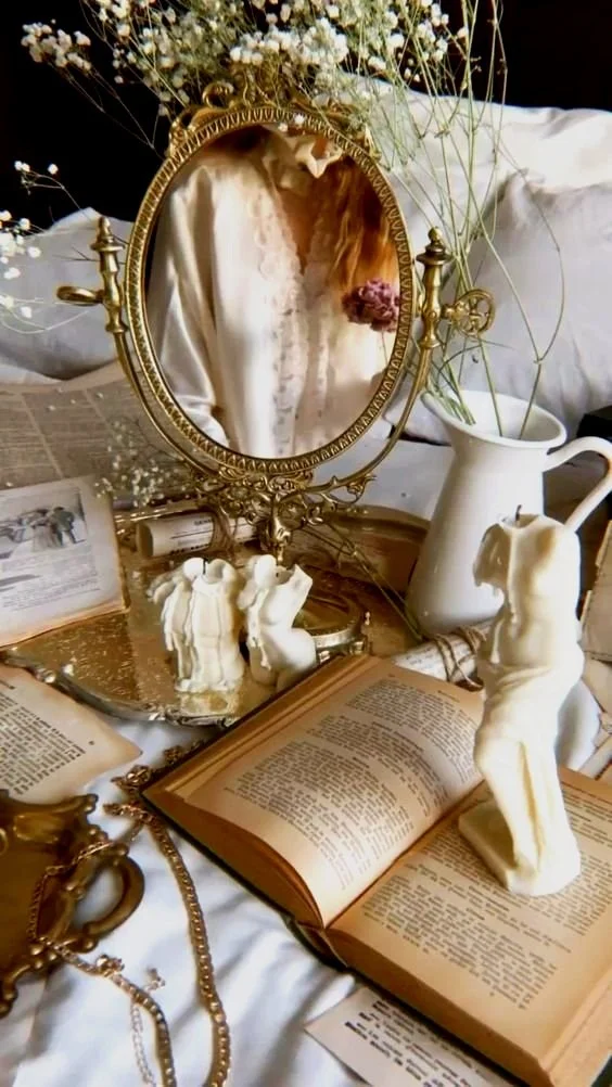Vintage mirror reflecting woman, open books, ceramic vase, figurines, dried flowers