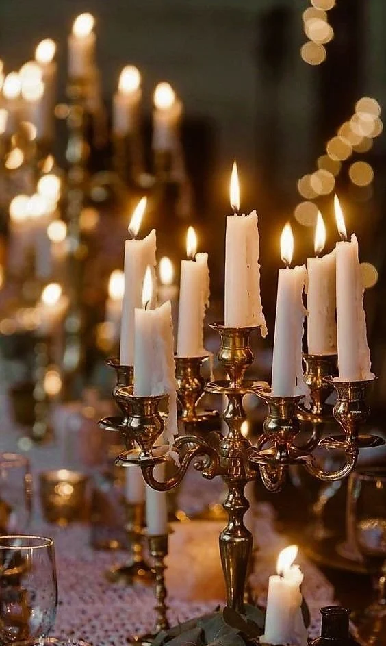 Romantic candlelit setting with multiple lit candles on ornate candelabras and string lights in the background.