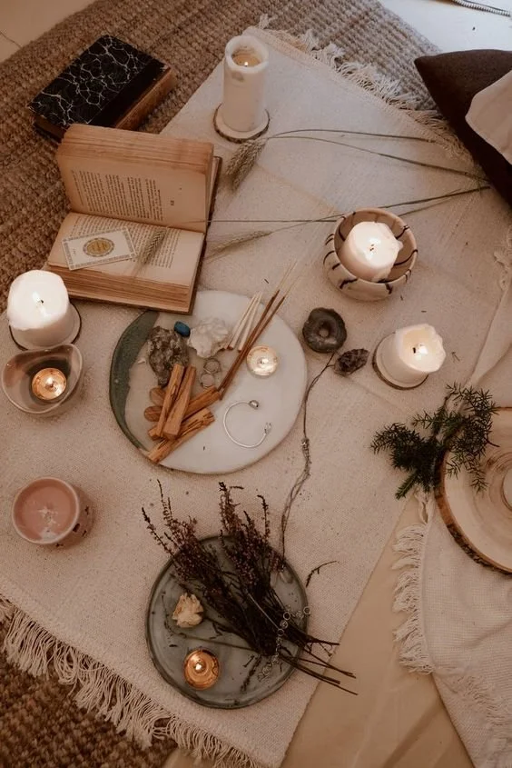 Cozy setup with candles, open book, crystals, and herbs on a textured rug.