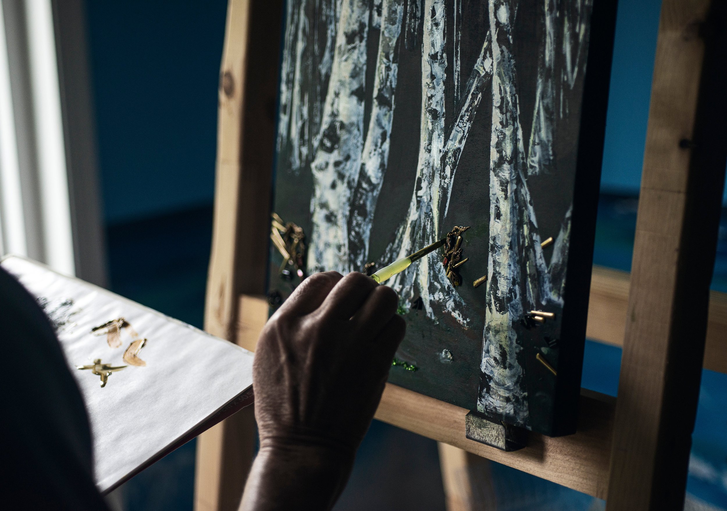 hand-holds-a-brush-to-canvas-painting-of-birch-trees.jpg