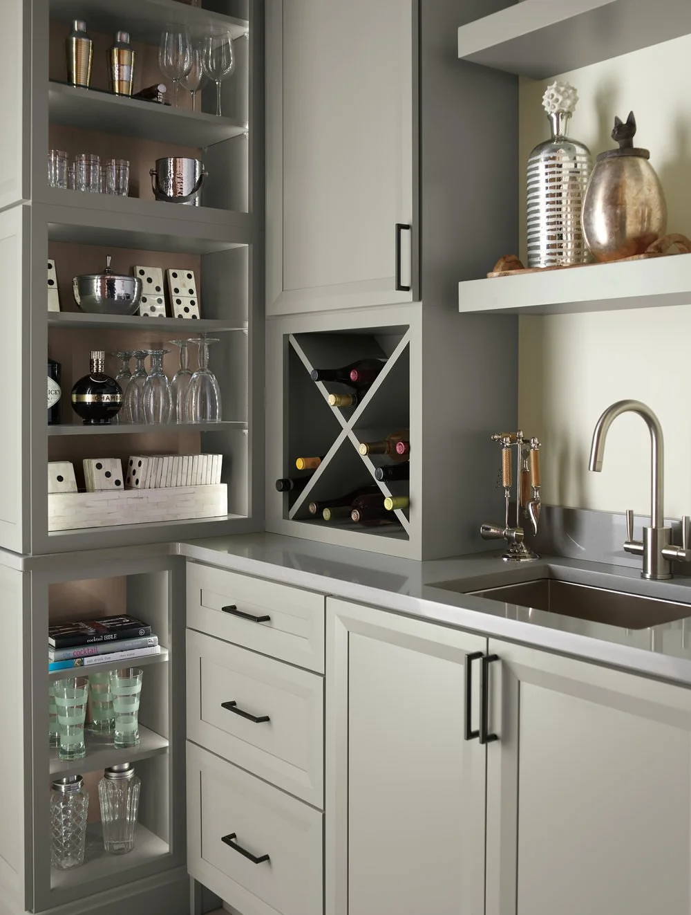 Kitchen with open shelves displaying glassware, wine bottles in a wine rack, books, and decorative items, with a sink and faucet.