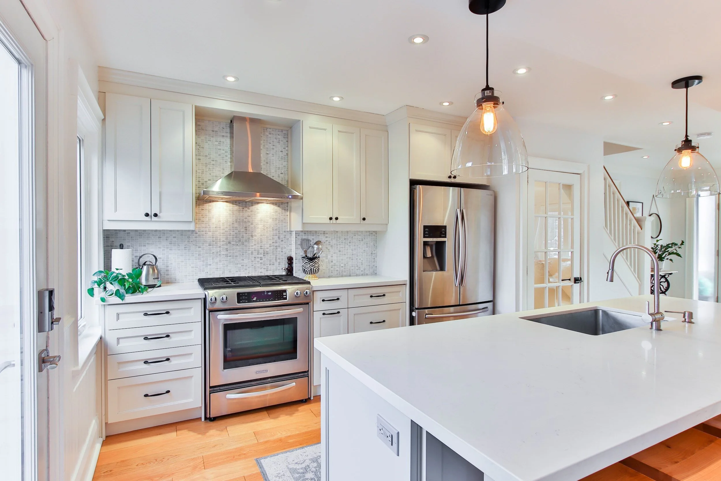 Modern kitchen with white cabinets, stainless steel appliances, a large island with a sink, pendant lighting, and hardwood floors.