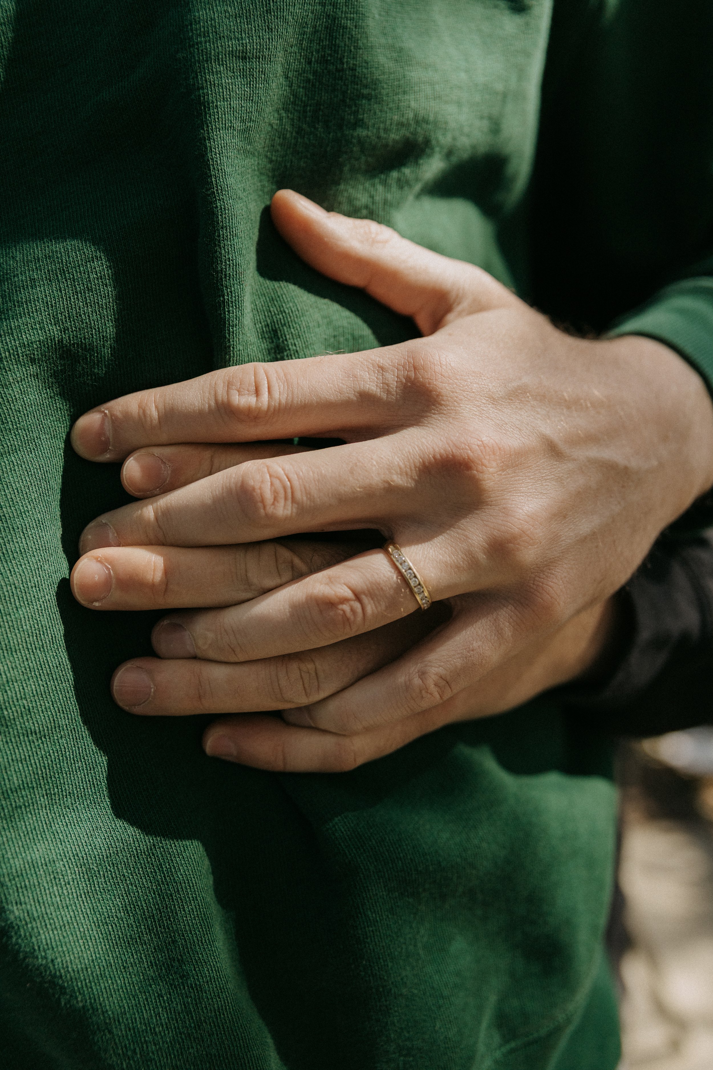 A person with light skin wearing a gold ring on their ring finger places their hand over a green fabric surface, possibly a jacket or sweater.