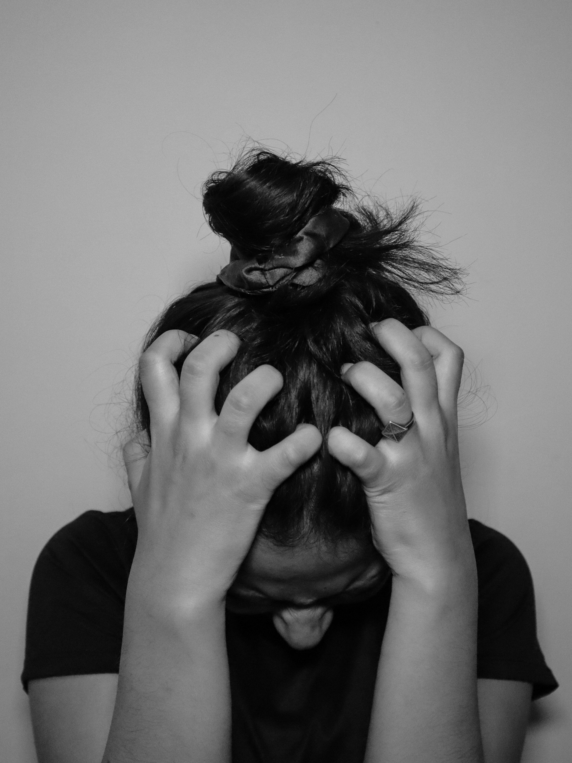 Person with dark hair holding their head with both hands, fingers intertwined, in front of a plain wall. Who may benefit from a from therapy provided by Empowering Hope and our skilled therapists.