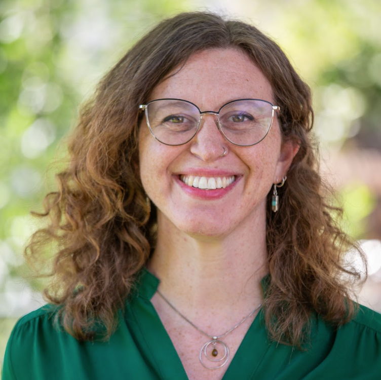 Emily, a therapist at Empowering Hope, with brown curly hair, glasses in a green top who is focused on supporting the neuro diverse community, trauma, anxiety, and grief/loss