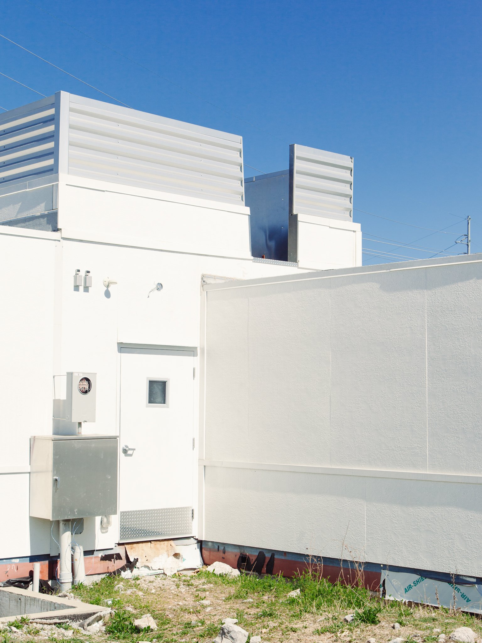 Close-up of a modern white building with vents and utility boxes against a clear blue sky.