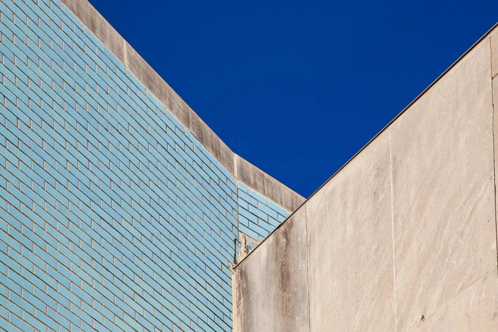 Close-up of modern building with blue brick wall, light-colored concrete wall, and clear blue sky.