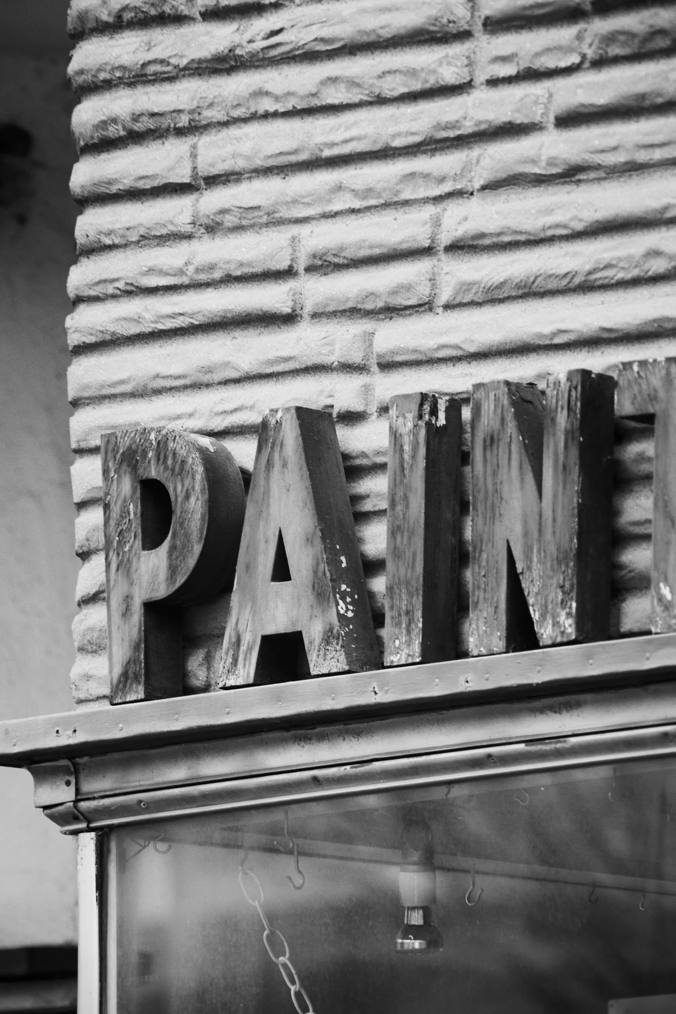Close-up of a textured brick wall with large wooden letters attached to it, partially visible. The letters spell out part of the word"PANEL." The image is in black and white.