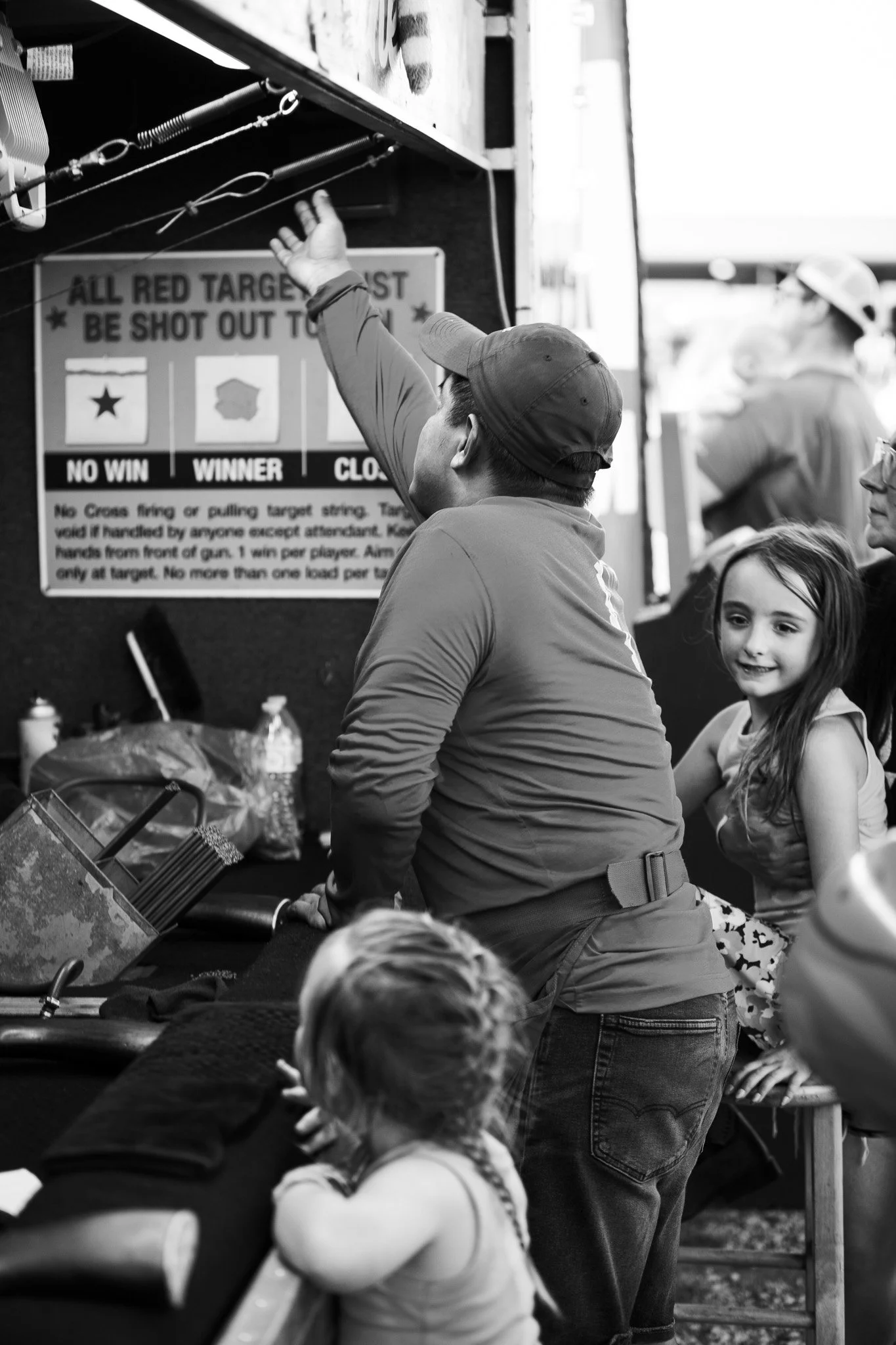 A group of children and adults at a shooting range, with some aiming at targets and others observing, in a black and white photo.