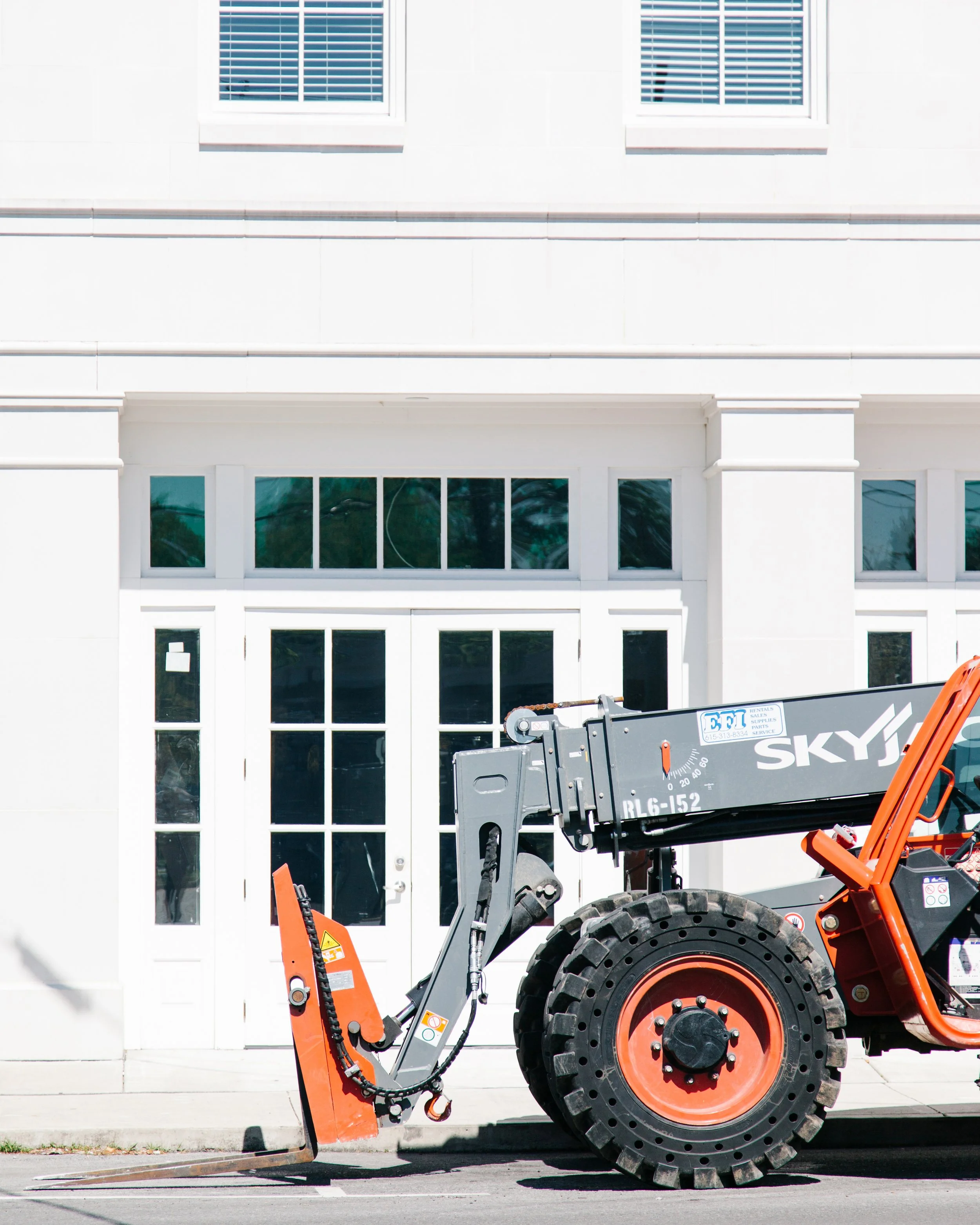 Construction lift equipment in front of a white building with windows featuring white blinds.