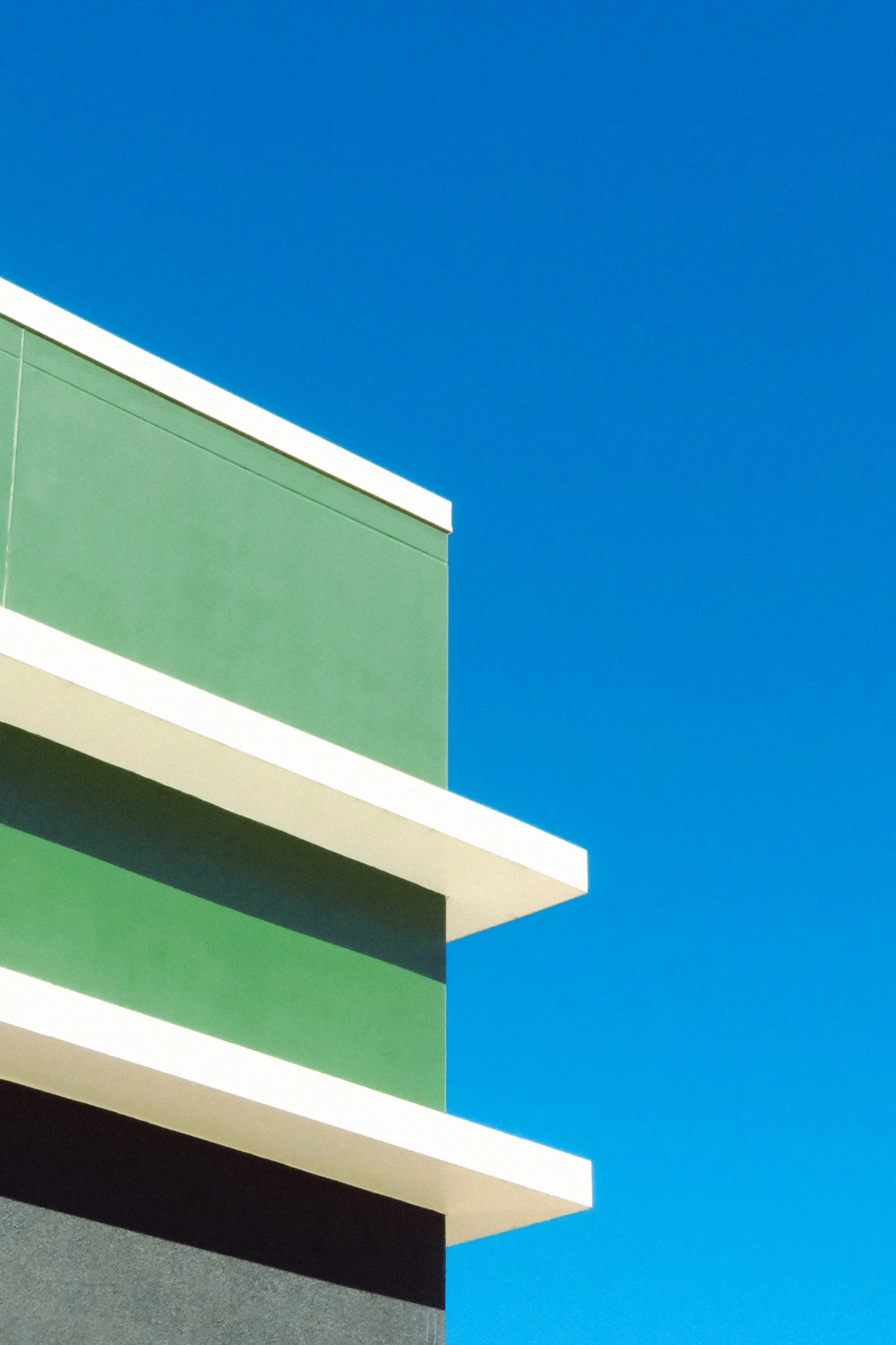 Close-up view of a modern building with green, white, and black sections, against a clear blue sky.