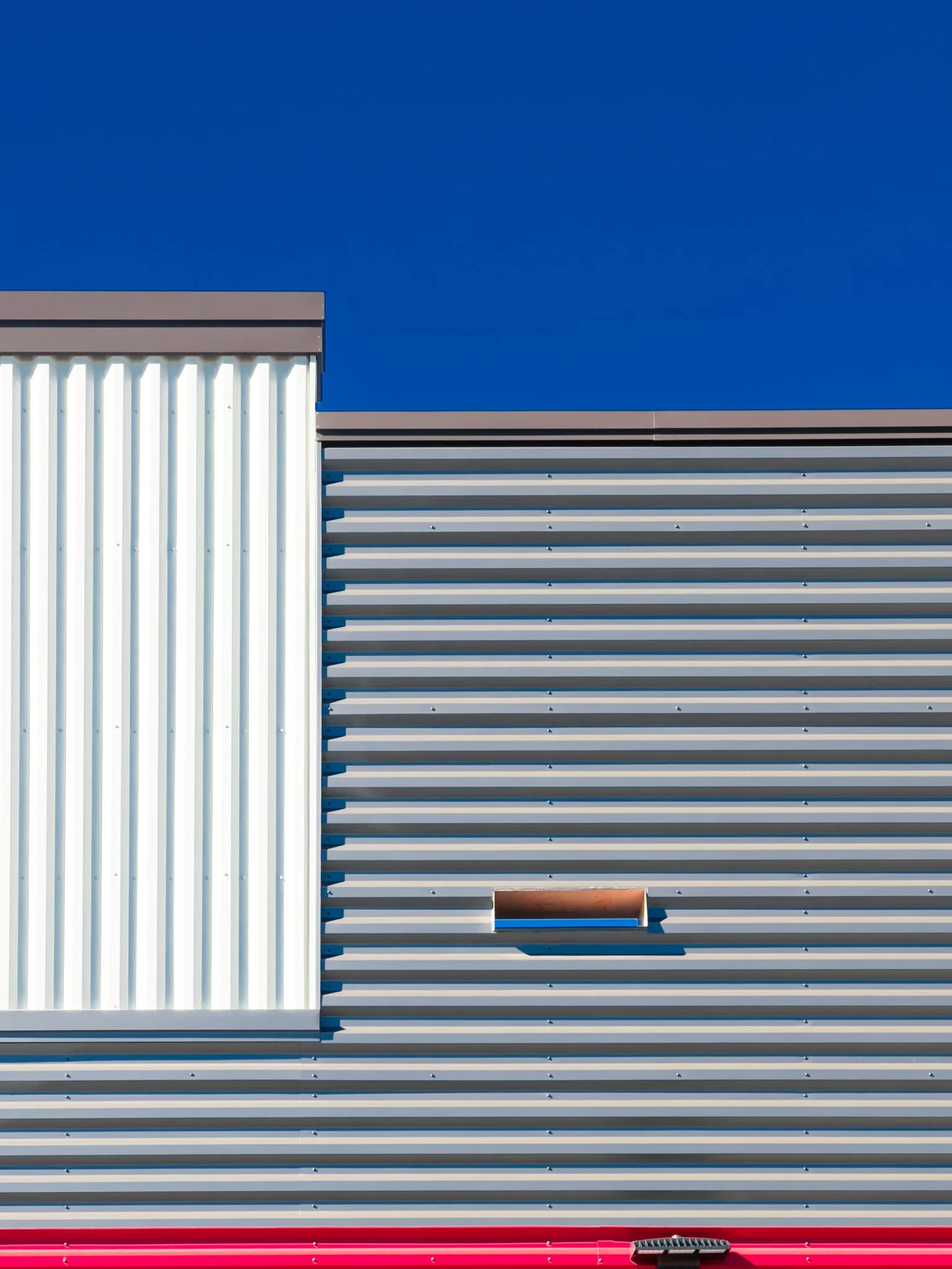 Close-up of modern building exterior with white and gray horizontal and vertical metal paneling against a clear blue sky.