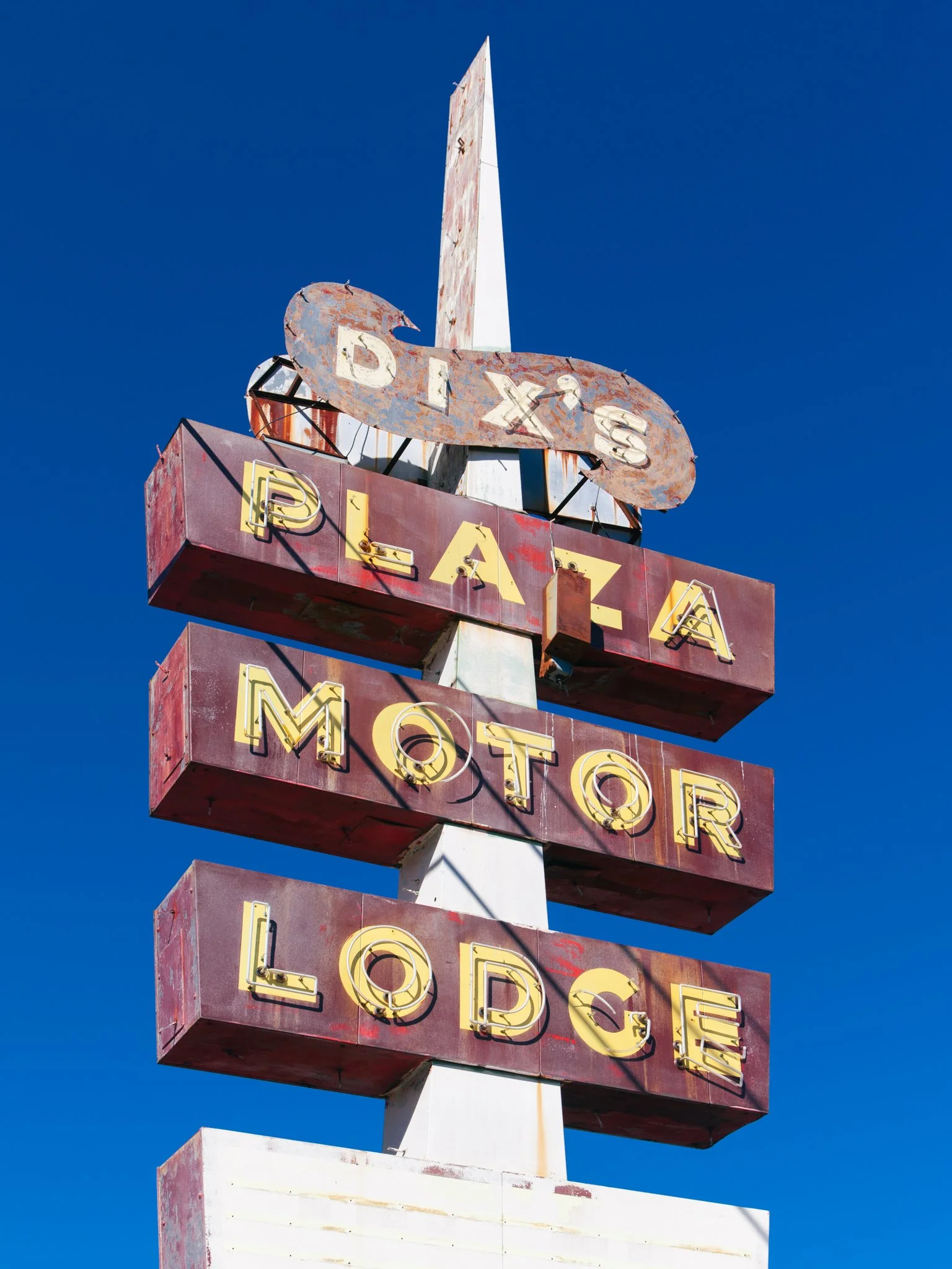 Old, rusted vintage sign with the words "Dixie" and "Bar" and neon lights, against a clear blue sky.