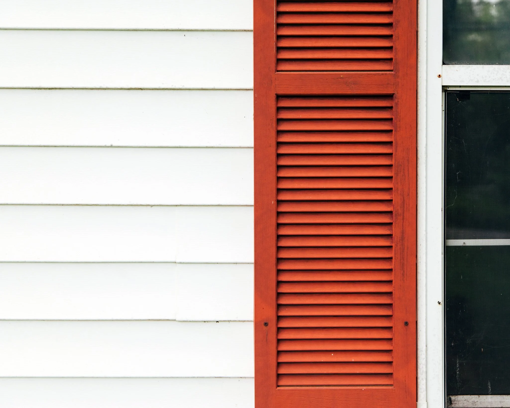 Side of a house showing white horizontal siding and a red louvered vent next to a glass window.