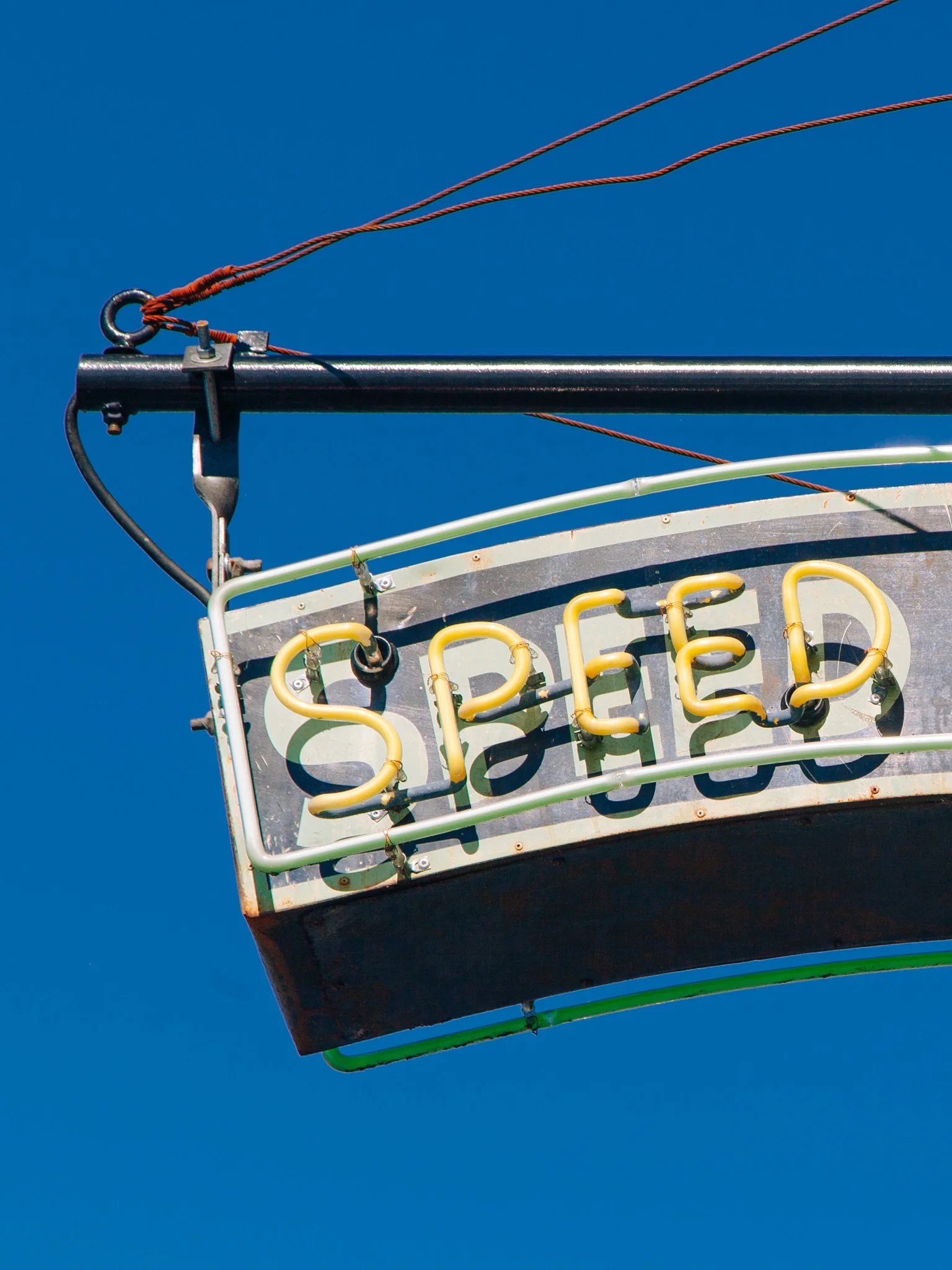 Close-up of a Ferris wheel gondola against a bright blue sky, partially visible at the bottom with yellow and green accents.