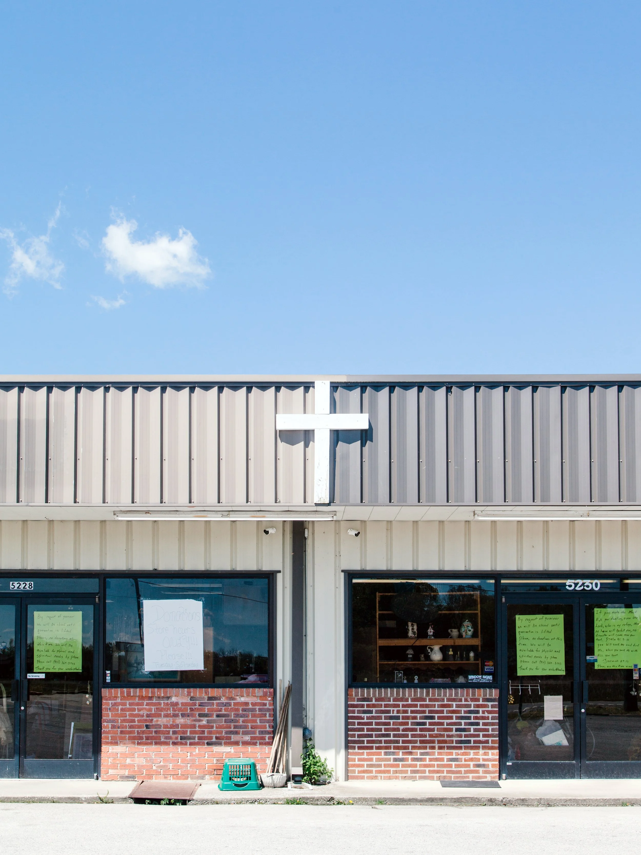Front view of a commercial building with two glass doors, a brick lower wall, and a metal upper wall, with signs and notices on the doors.