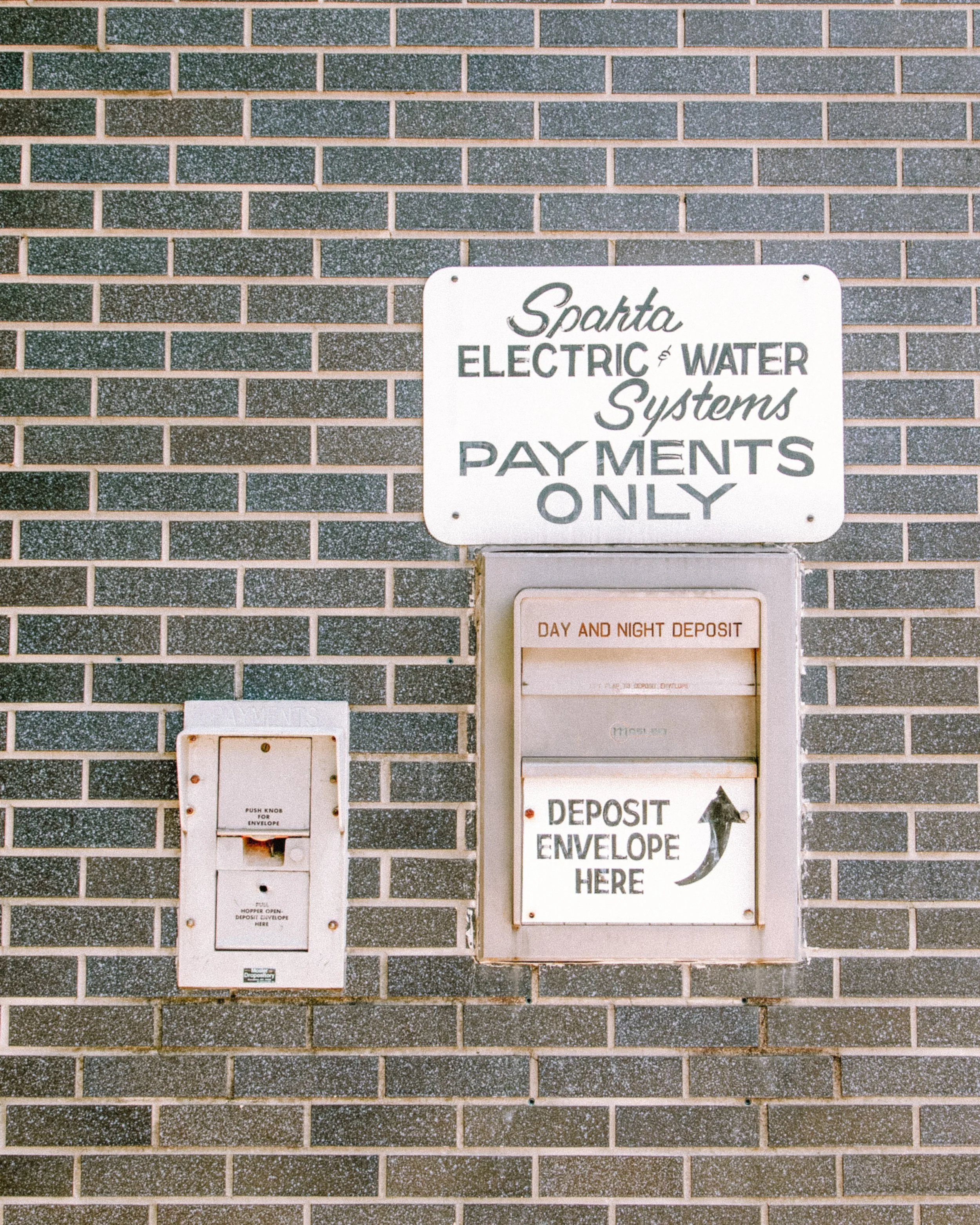 A brick wall with signs and mailboxes for a payment system, indicating methods for making deposits and payments only, with instructions for envelope deposits and coin slot usage.