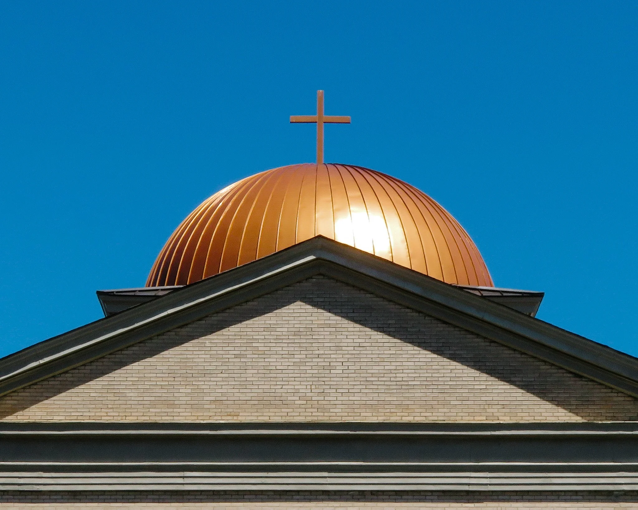 Close-up of a church steeple with a gold dome topped with a cross, against a clear blue sky.