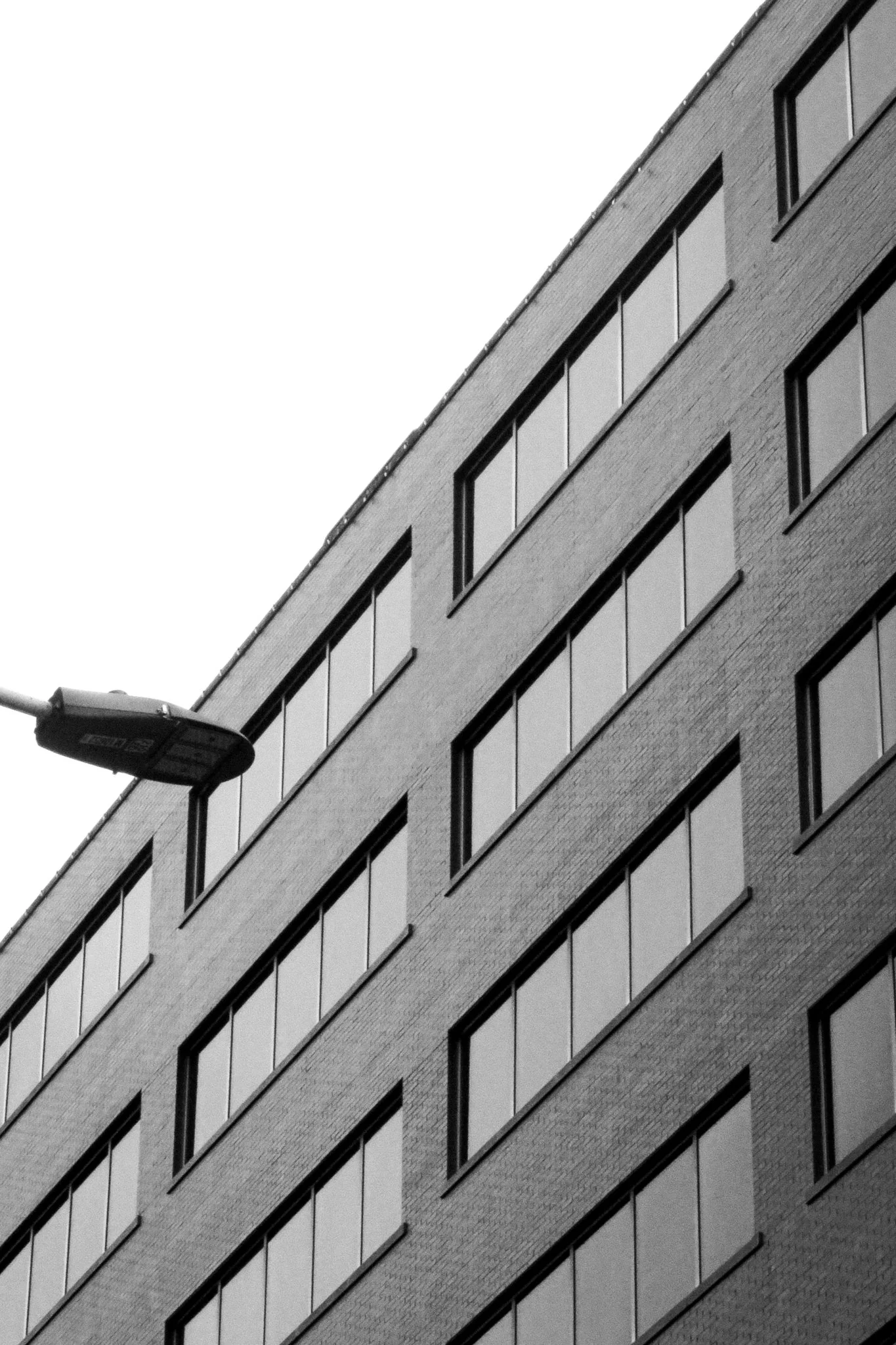 A black-and-white photo of a modern brick building with multiple windows and a street lamp in the foreground.