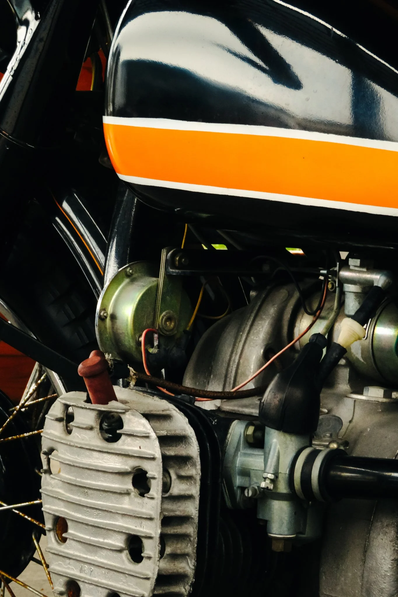 Close-up of a vintage motorcycle engine with a black fuel tank featuring orange and white stripes.