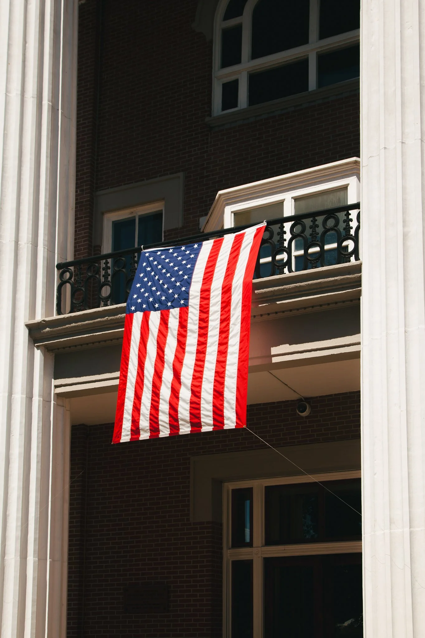 American flag hanging from a balcony of a building with brick and white columns.