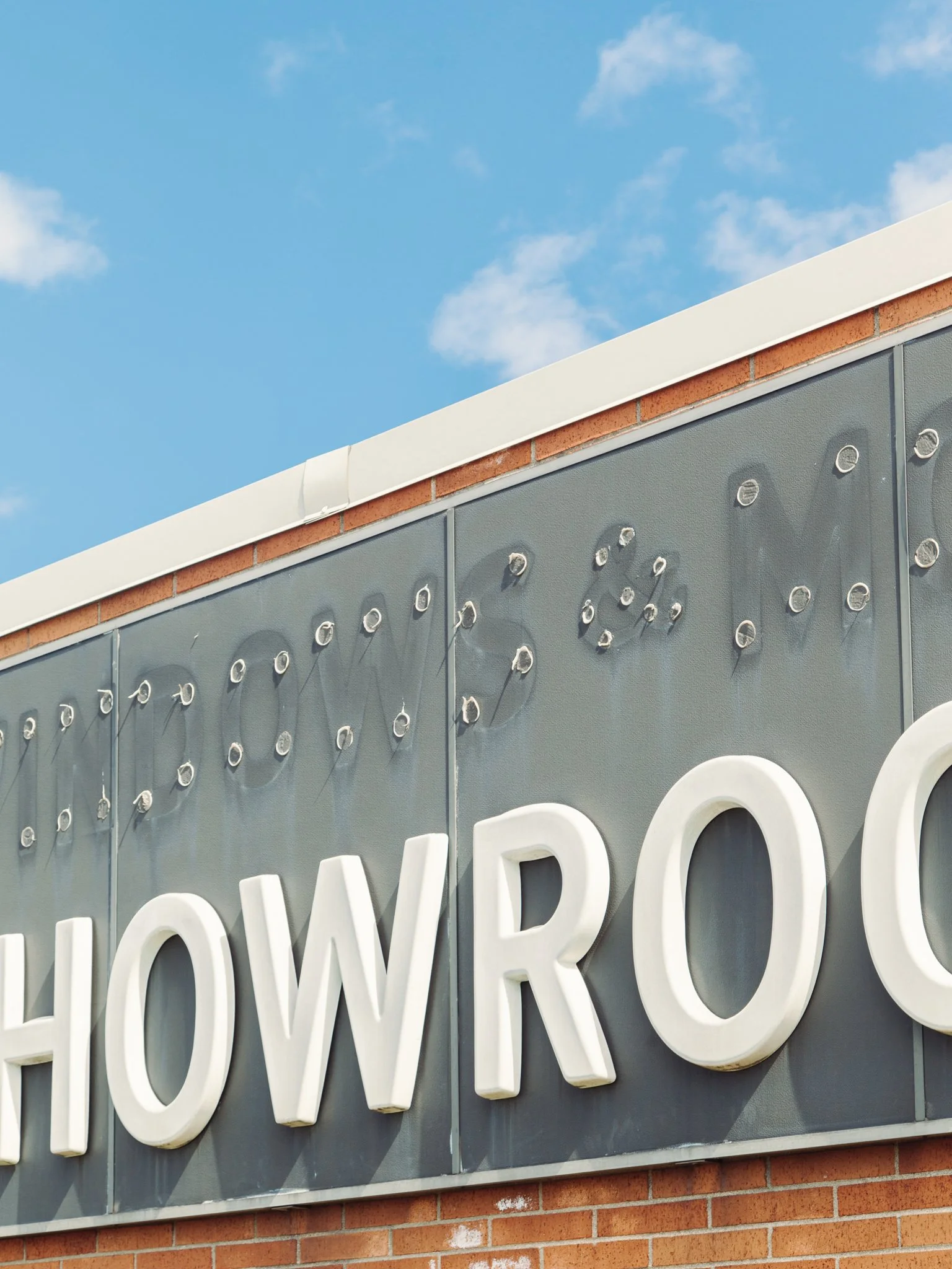 Partial view of a building exterior with white illuminated signage letters spelling 'OWER' and part of a large white letter 'D' visible below, against a backdrop of a clear blue sky with some clouds.