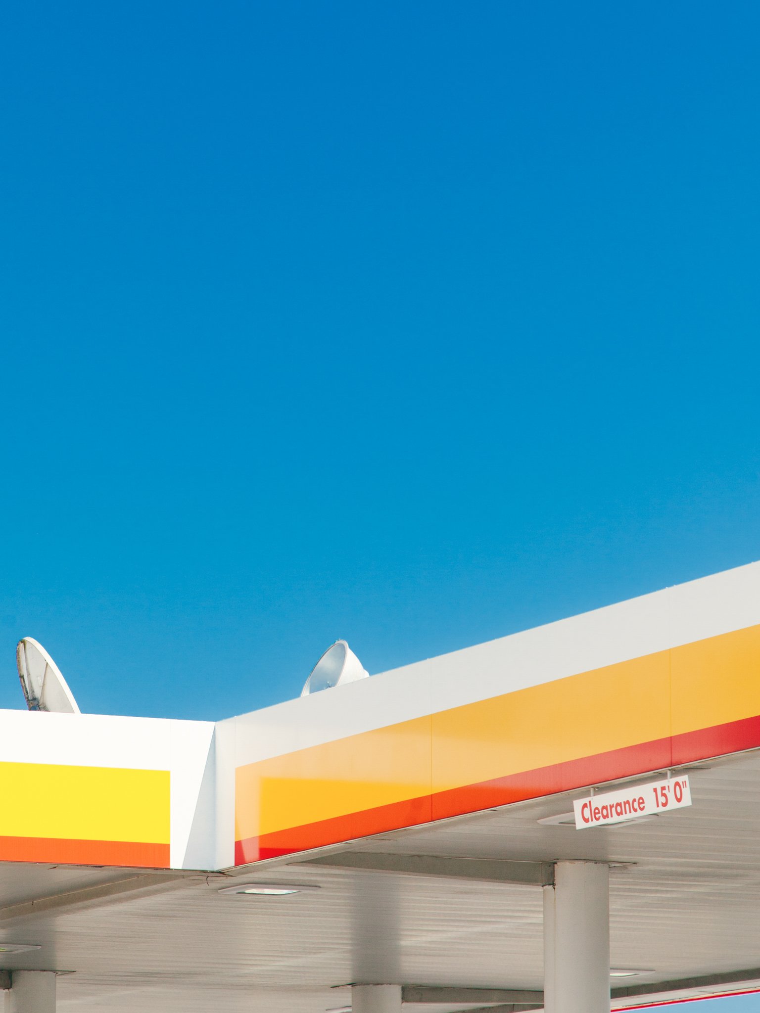 Colorful modern building with a blue sky background, featuring satellite dishes on the roof and a sign indicating a 15-foot clearance.