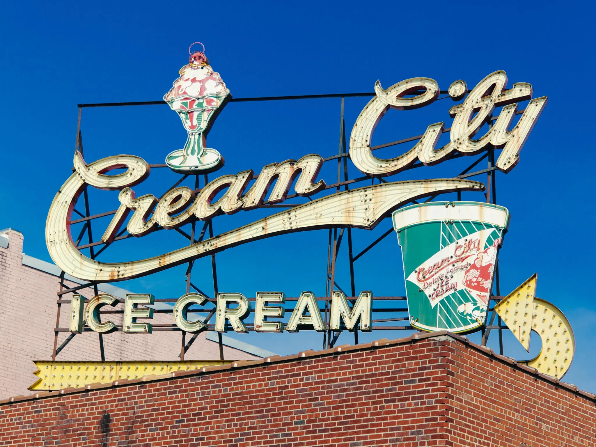 Sign advertising ice cream with a depiction of an ice cream sundae on top, against a clear blue sky.