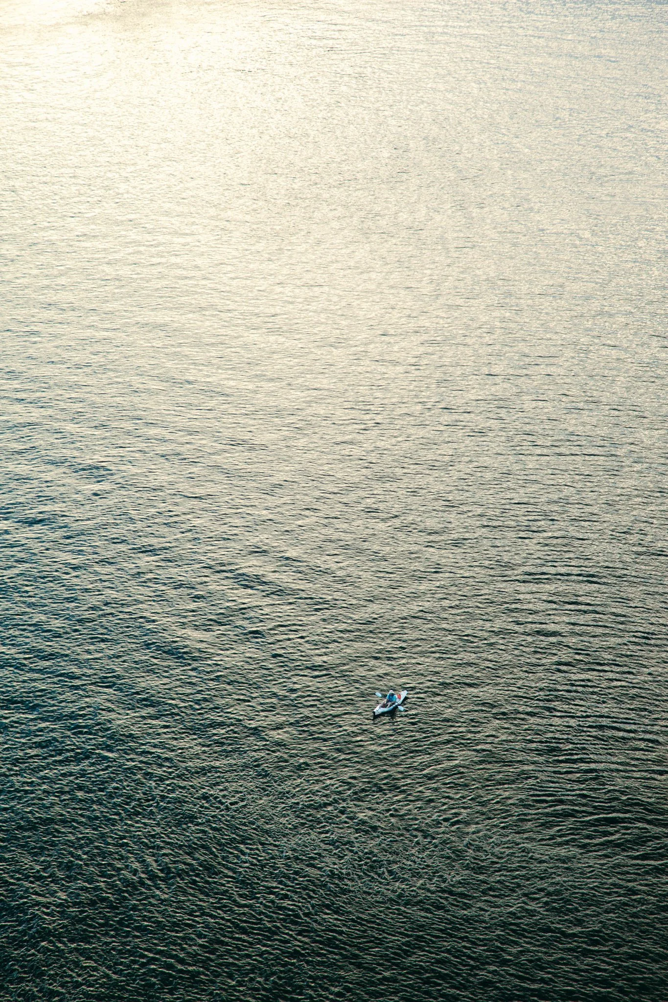 A small boat with two people on a large body of water, seen from above.