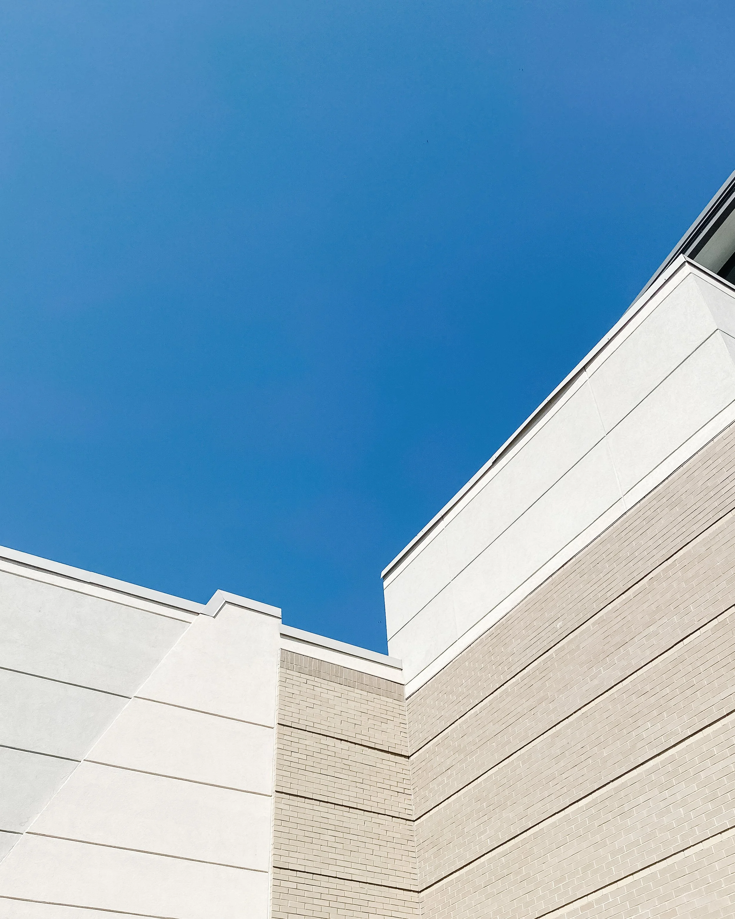 Closest corner of a modern white building with horizontal panels and brickwork, against a clear blue sky.