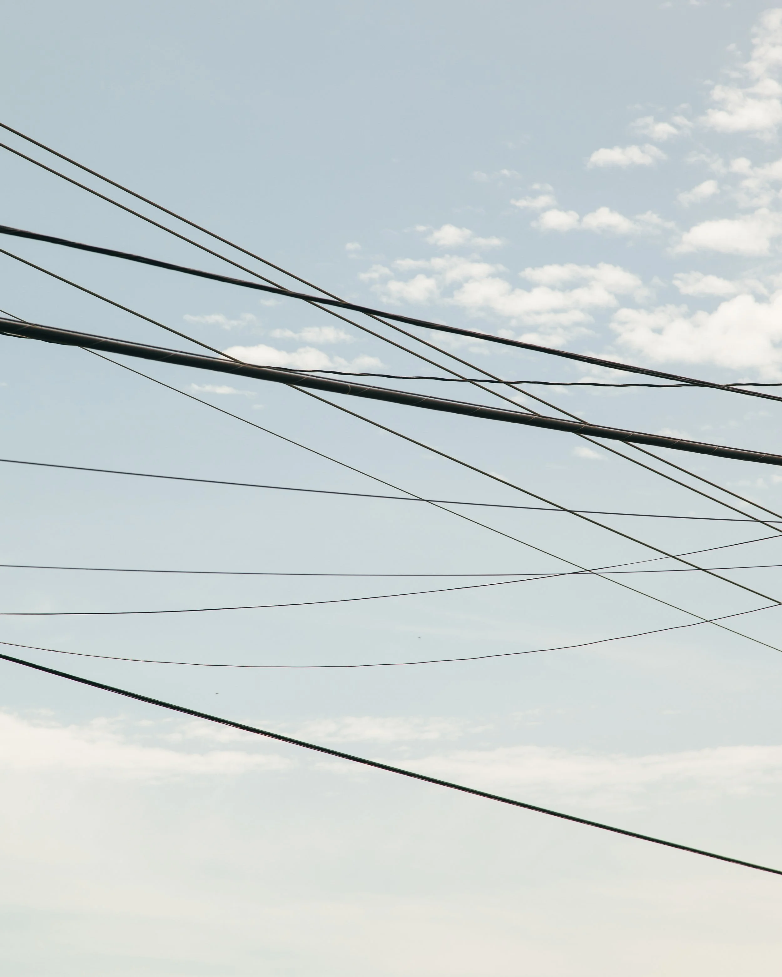 Multiple power lines crossing the sky with scattered clouds in the background.