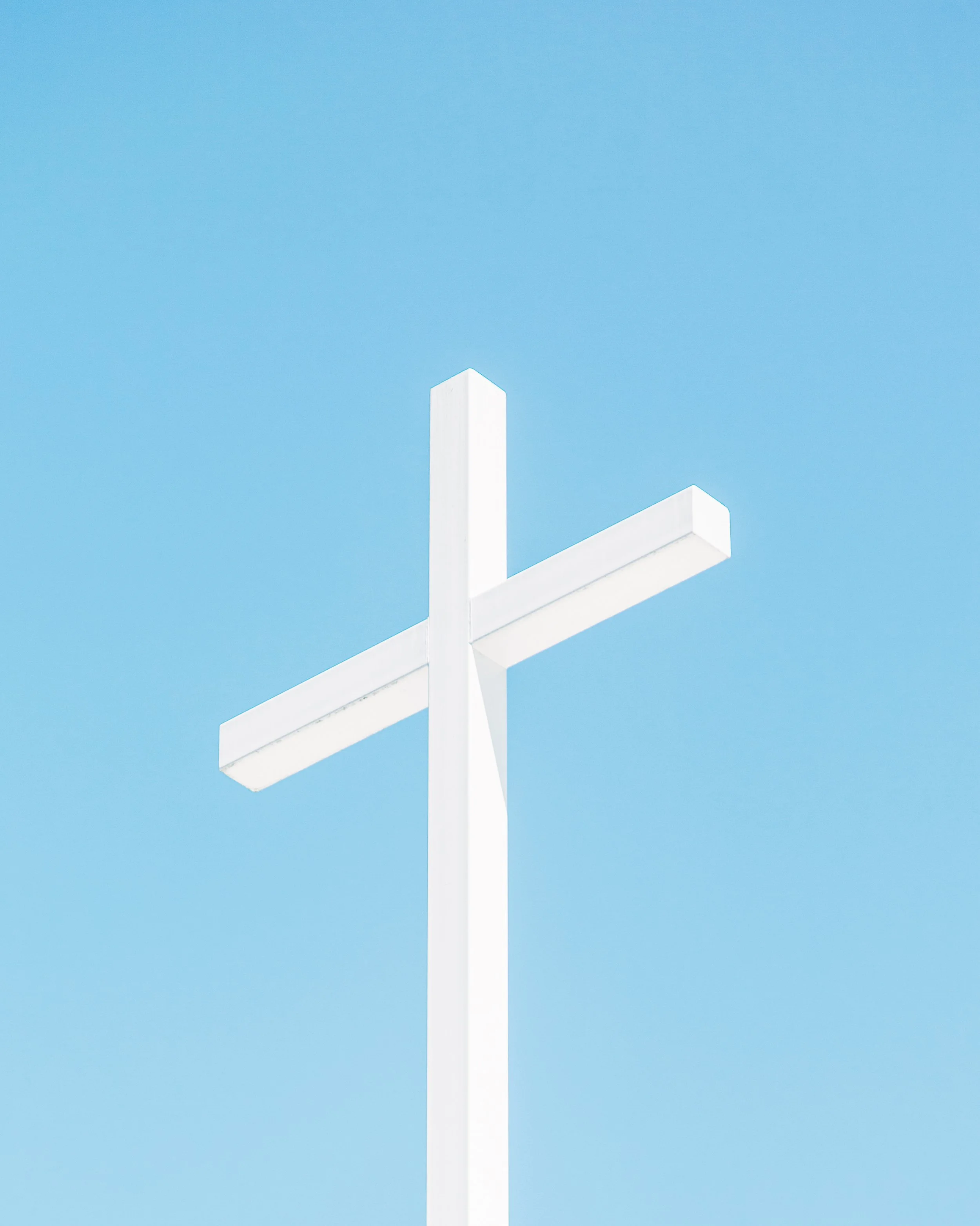 White modern geometric sculpture with sharp angles and clean lines against a clear blue sky.