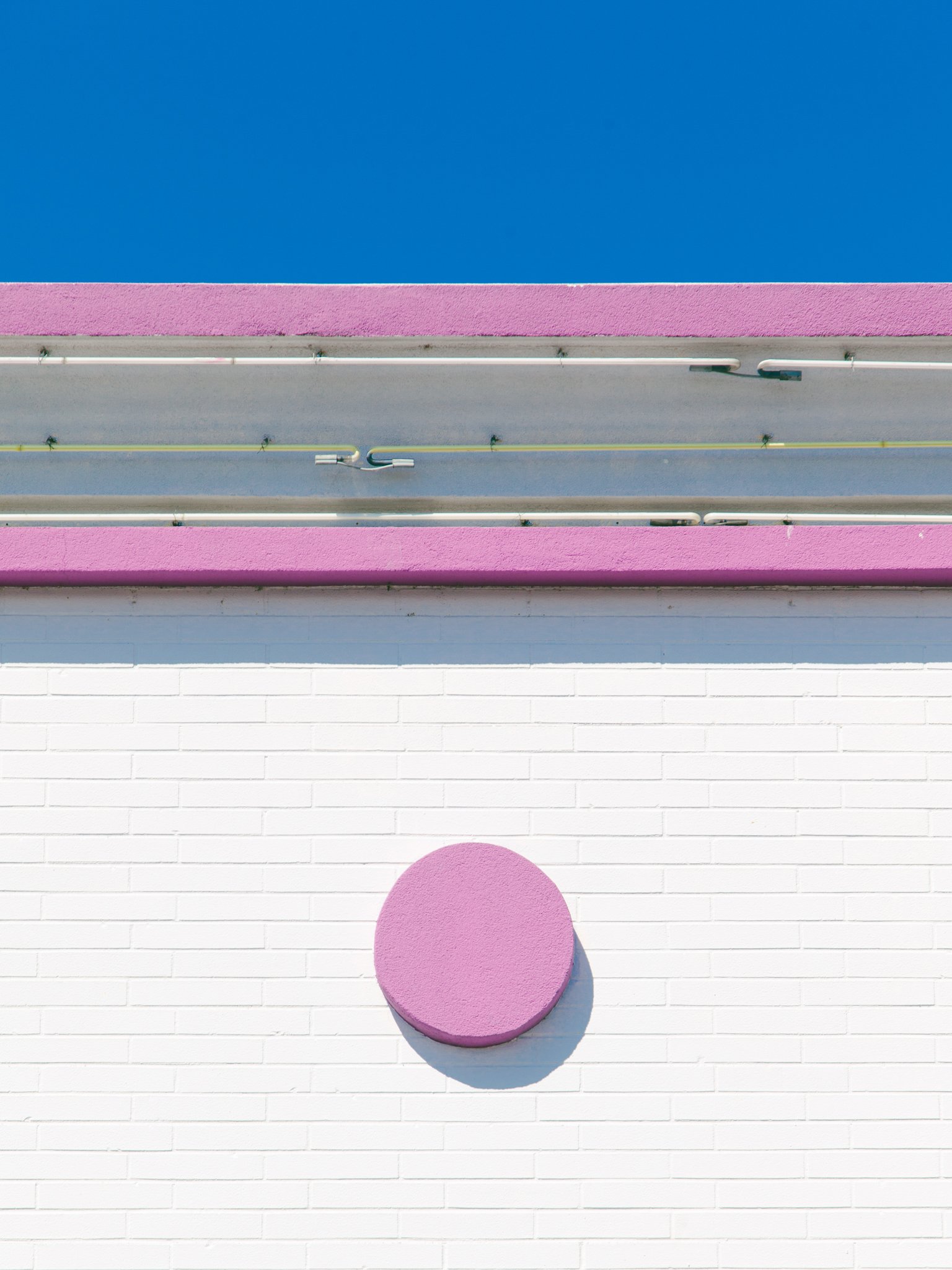 A pink circle on a white brick wall with purple horizontal stripes above it.