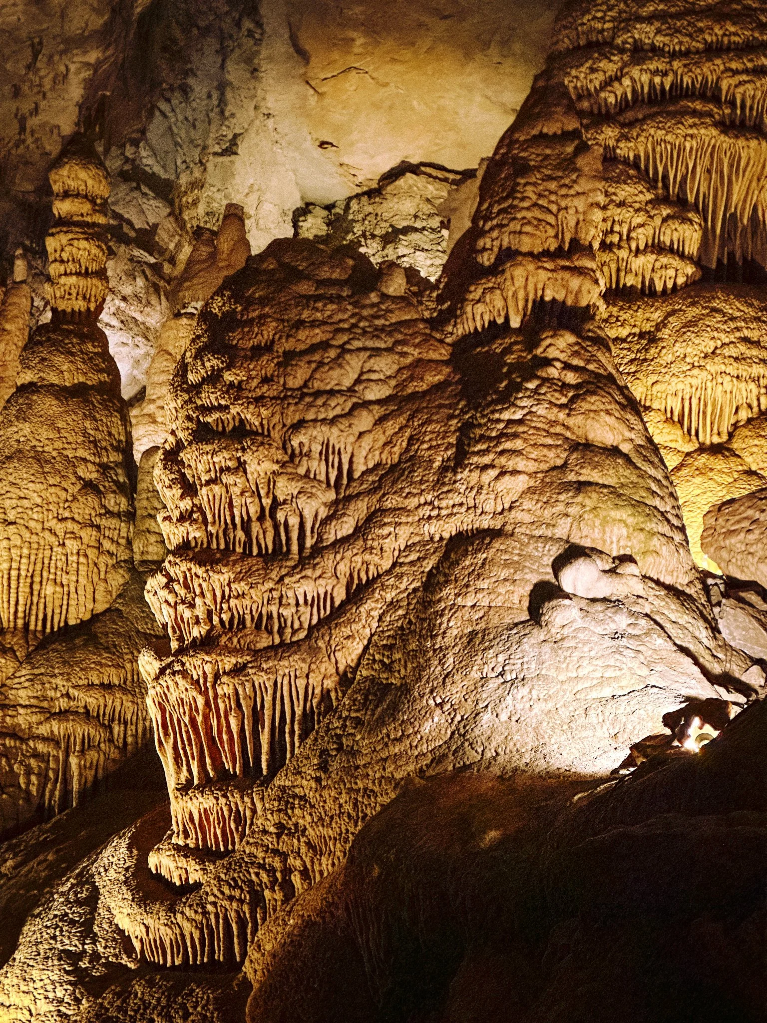 The image shows the interior of a cave with stalactites hanging from the ceiling and stalagmites rising from the ground, illuminated with warm lighting.