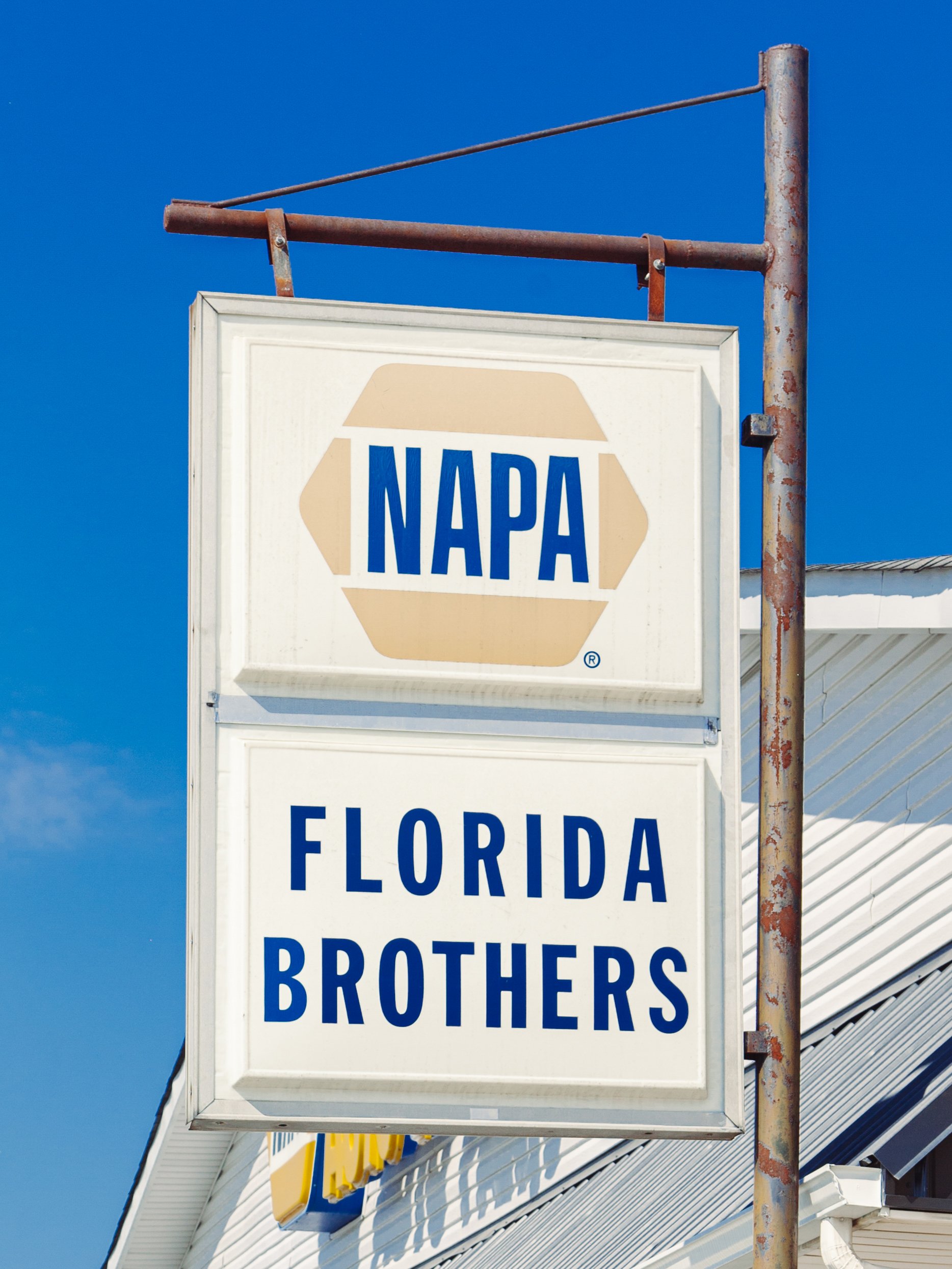 Sign for NAPA Brothers, located on a building with a metal roof, against a bright blue sky.