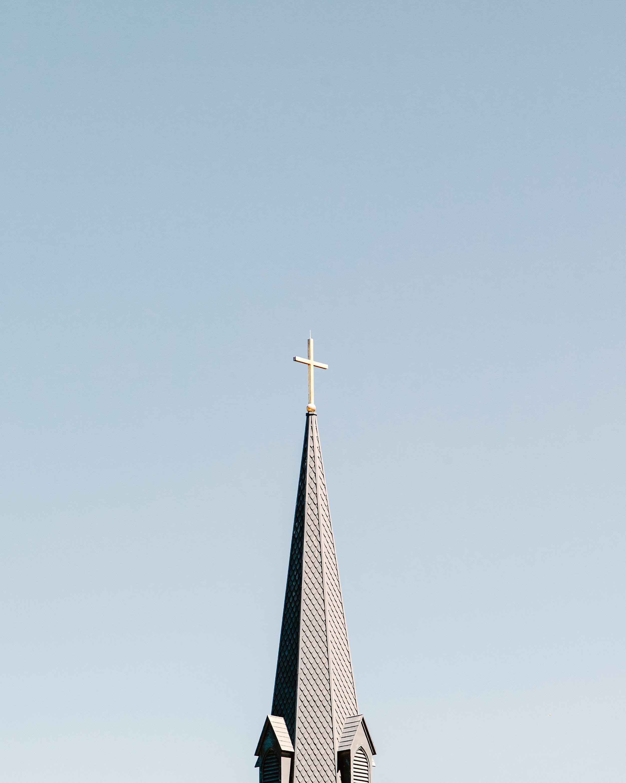 Church steeple with a cross on top against a clear blue sky.