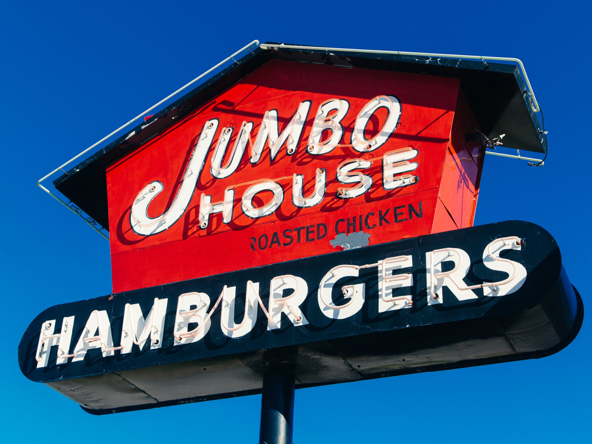 Close-up of a vintage neon sign for Jimmy's House, a fried chicken restaurant, against a clear blue sky.