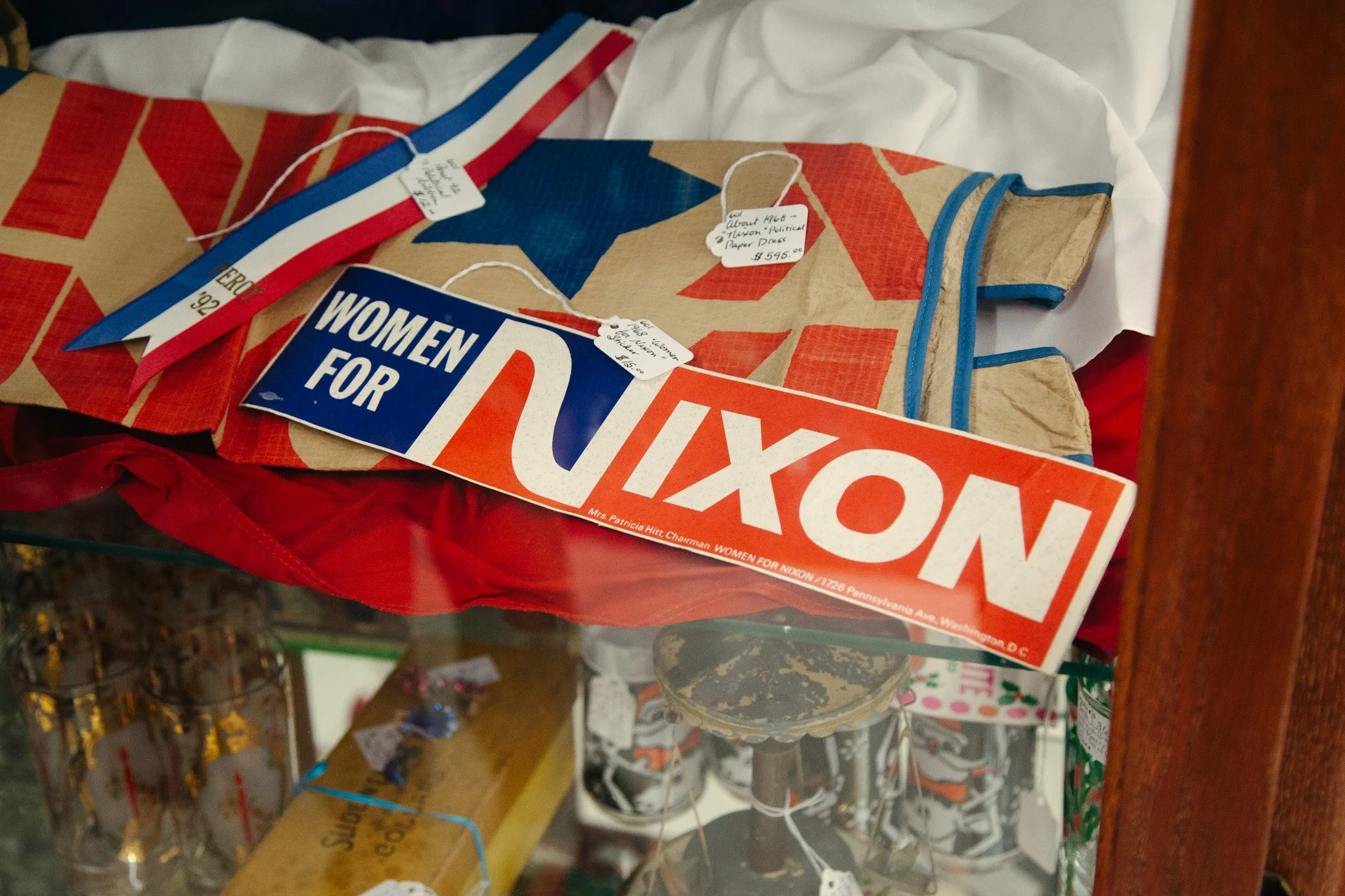 Various fireworks boxes and packages stored on a shelf, including a 'Women for Nixon' campaign sticker and handwritten price tags on some of the packages.