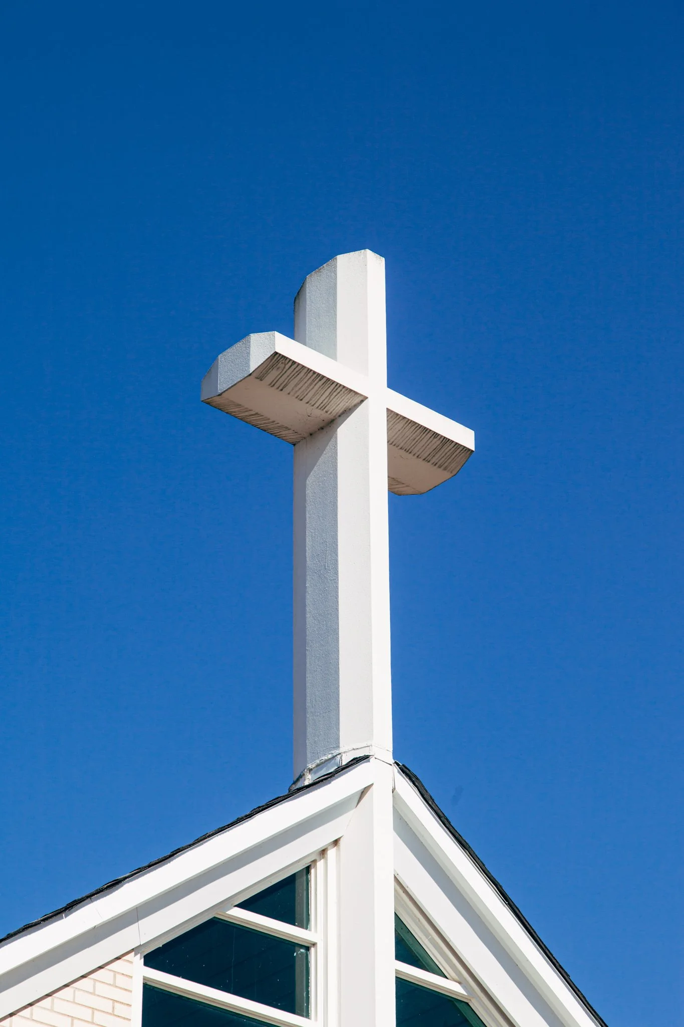 White house roof with a cross-shaped weather vane on top, clear blue sky background.