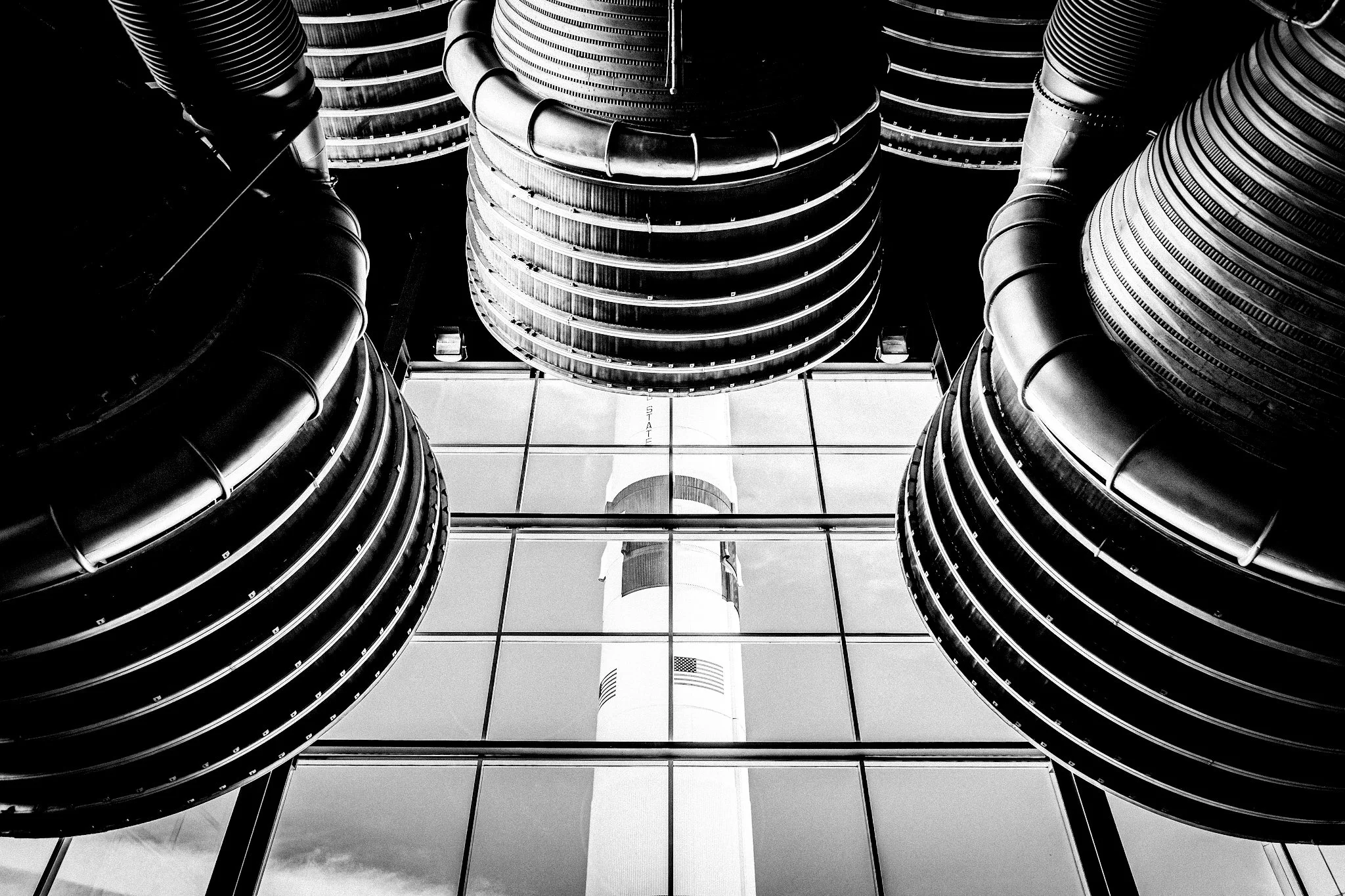 Black and white photo of modern building with rounded, layered metal turbines, and a glass windowed wall in the background