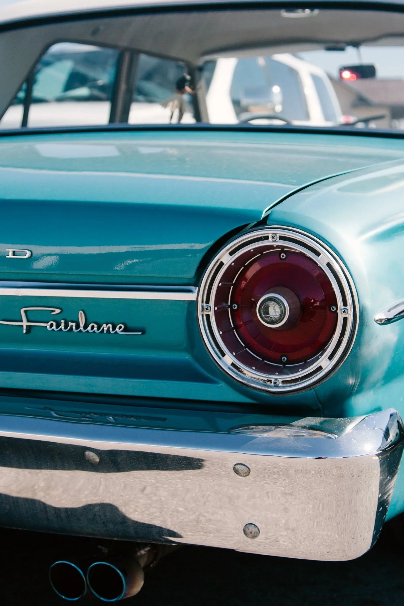 Close-up of the rear of a vintage teal-colored Ford Fairlane car, showing the tail light and exhaust pipes.