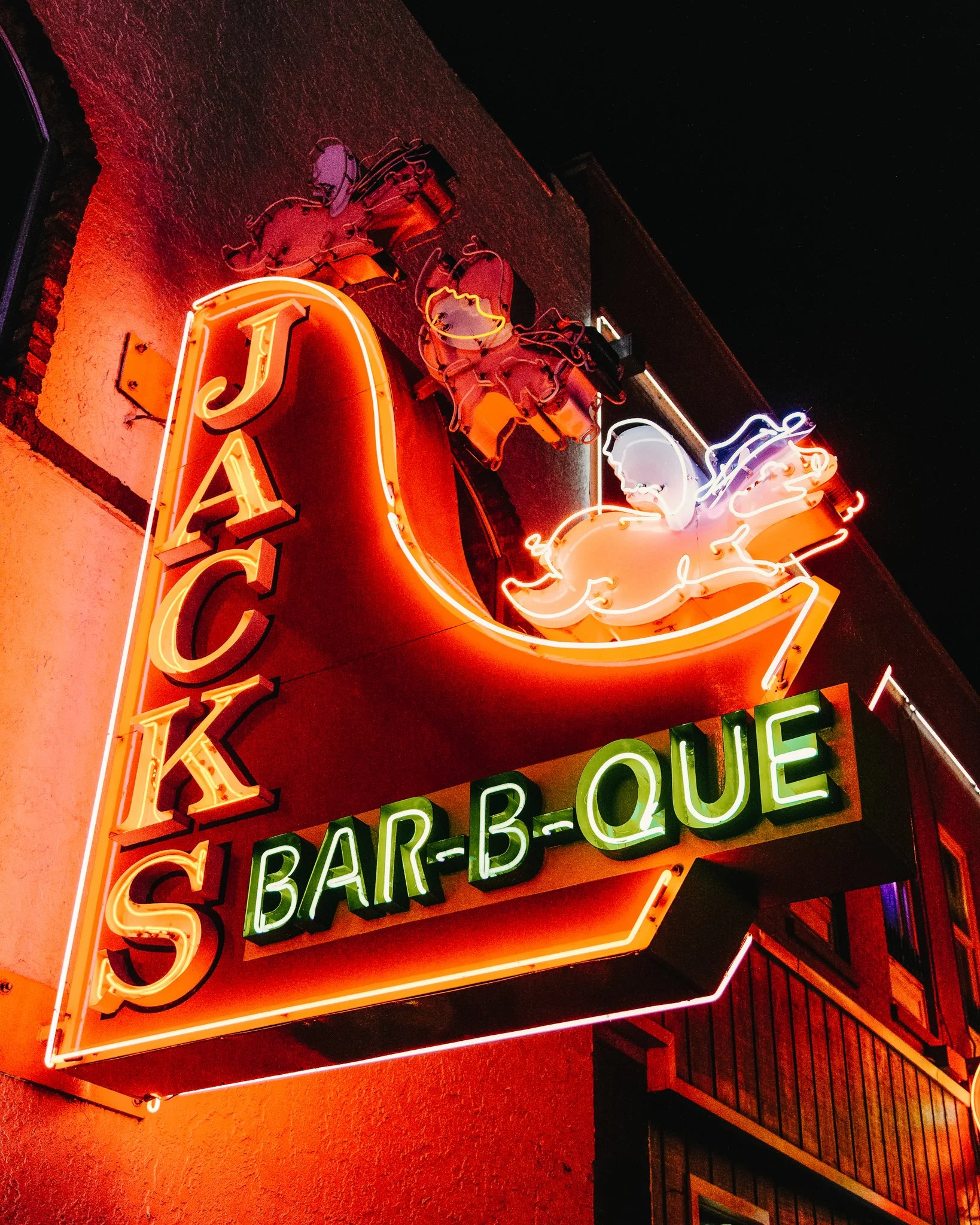 Neon sign advertising a bar-b-que with images of pigs, a chef, and neon lighting in various colors.