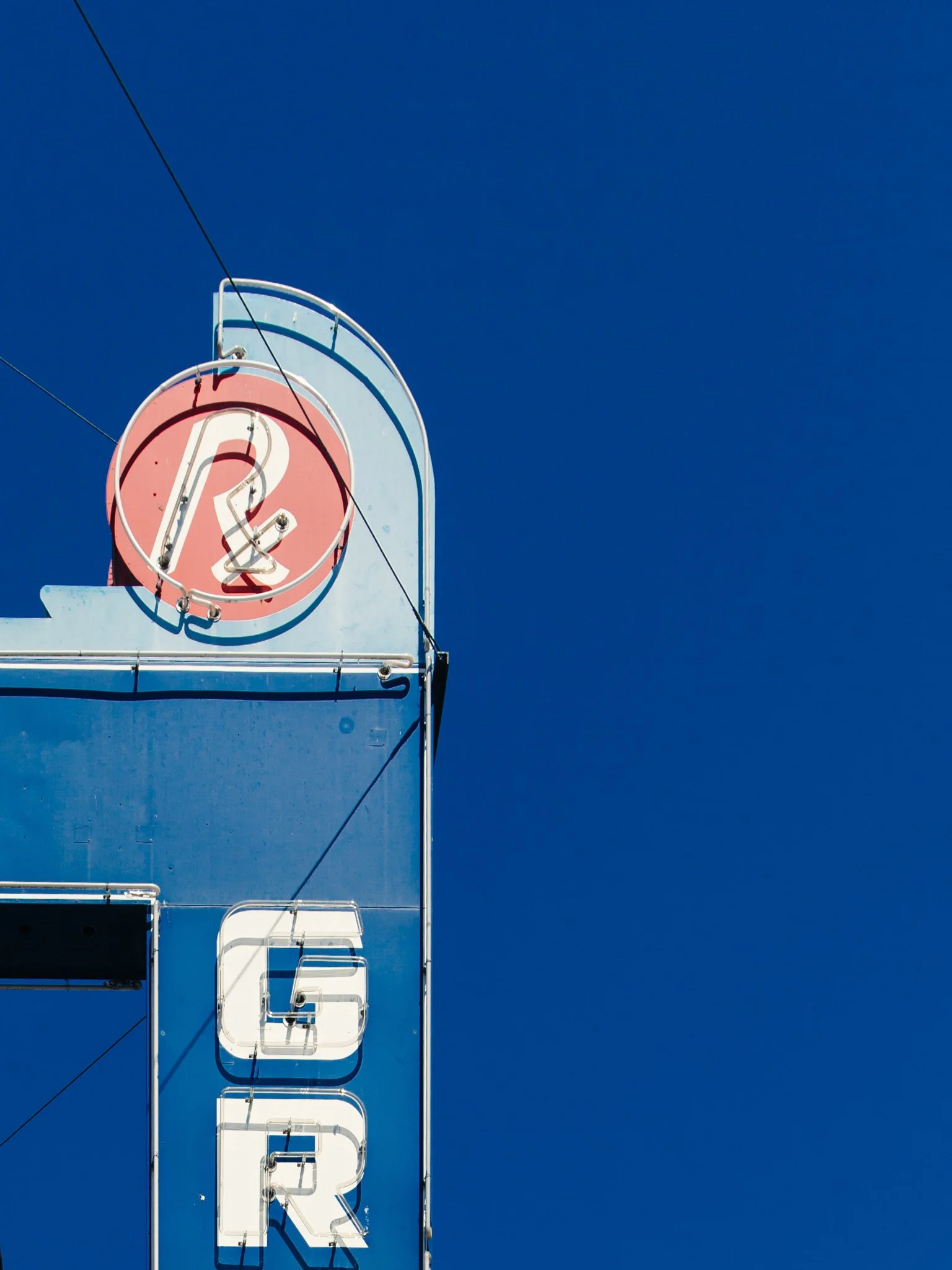 Close-up of a vintage neon sign with the word 'THE' at the top and partly visible letters below, against a clear blue sky.
