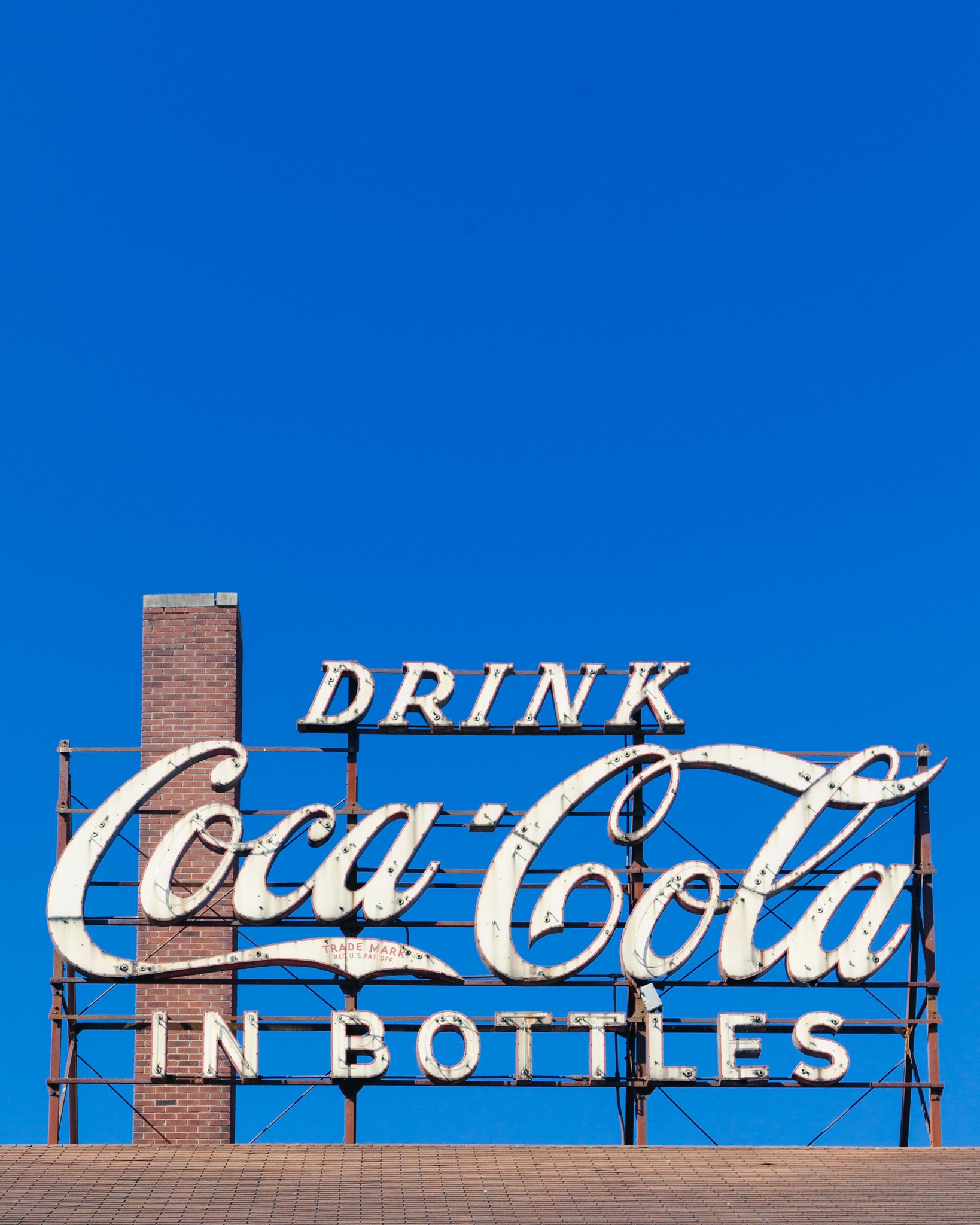 Sign for a drive-in restaurant with a brick chimney and a building with a shingle roof.