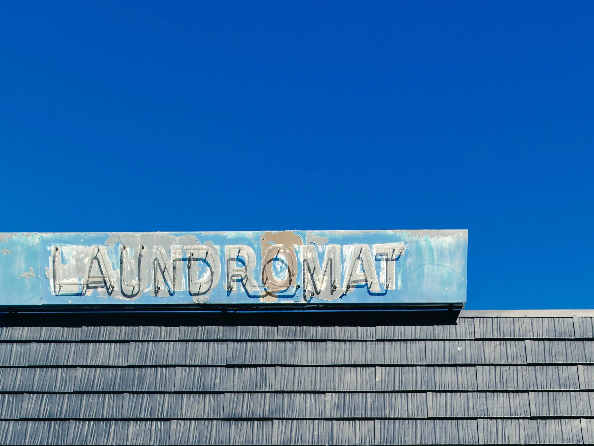 Old weathered neon sign on a building with a blue sky background, reading 'UND' and partially visible text 'useum'.